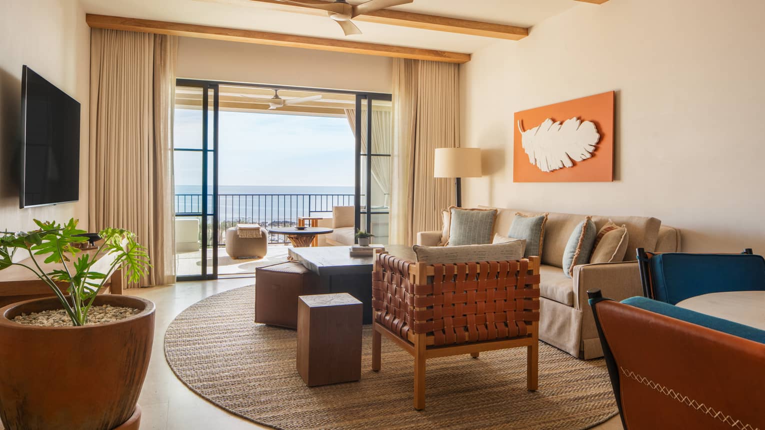 Stylish hotel suite living room with sofa and arm chair, opening to ocean-view balcony