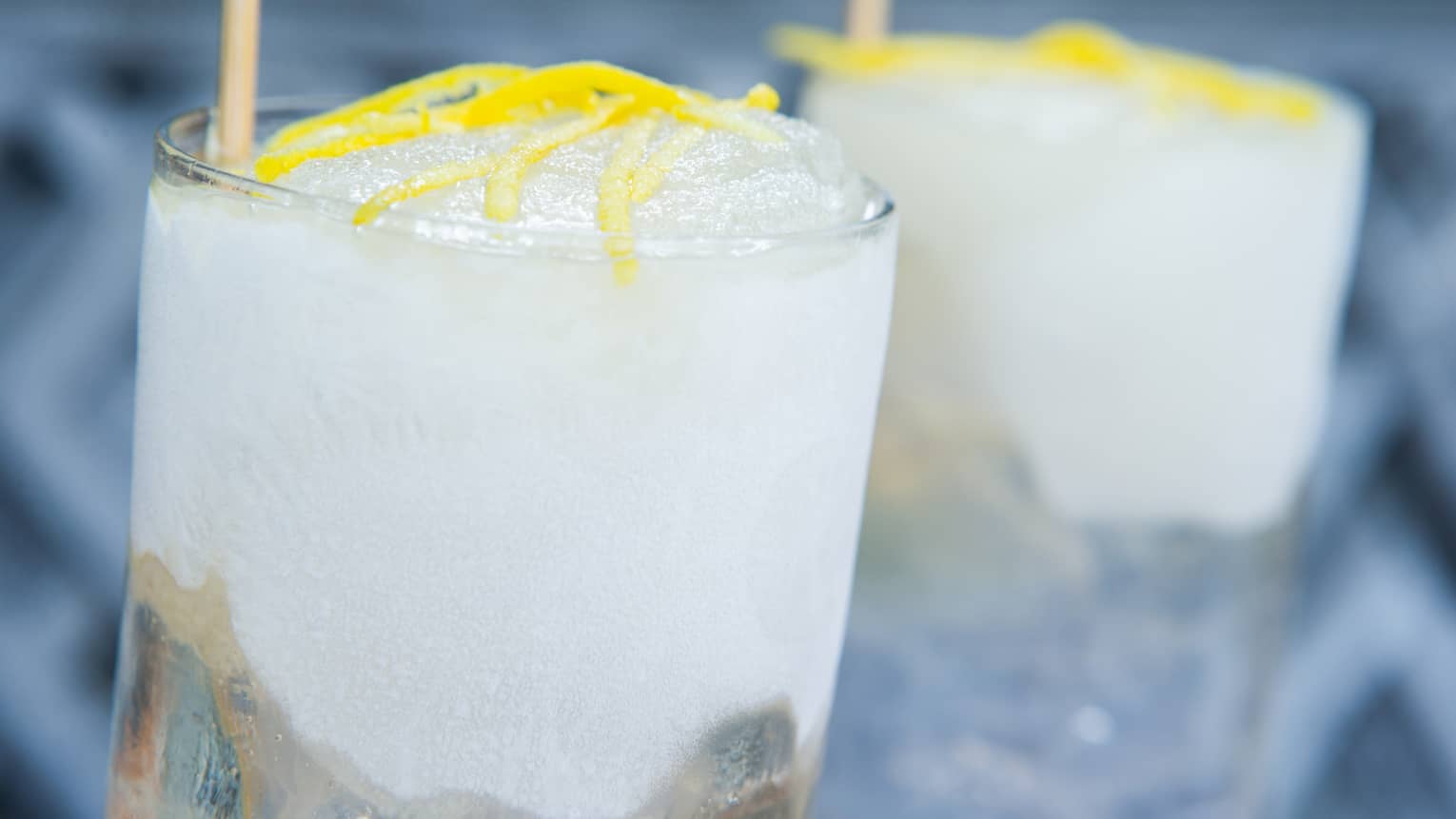 Close-up of crushed ice cocktails in tall glasses garnished with lemon rinds