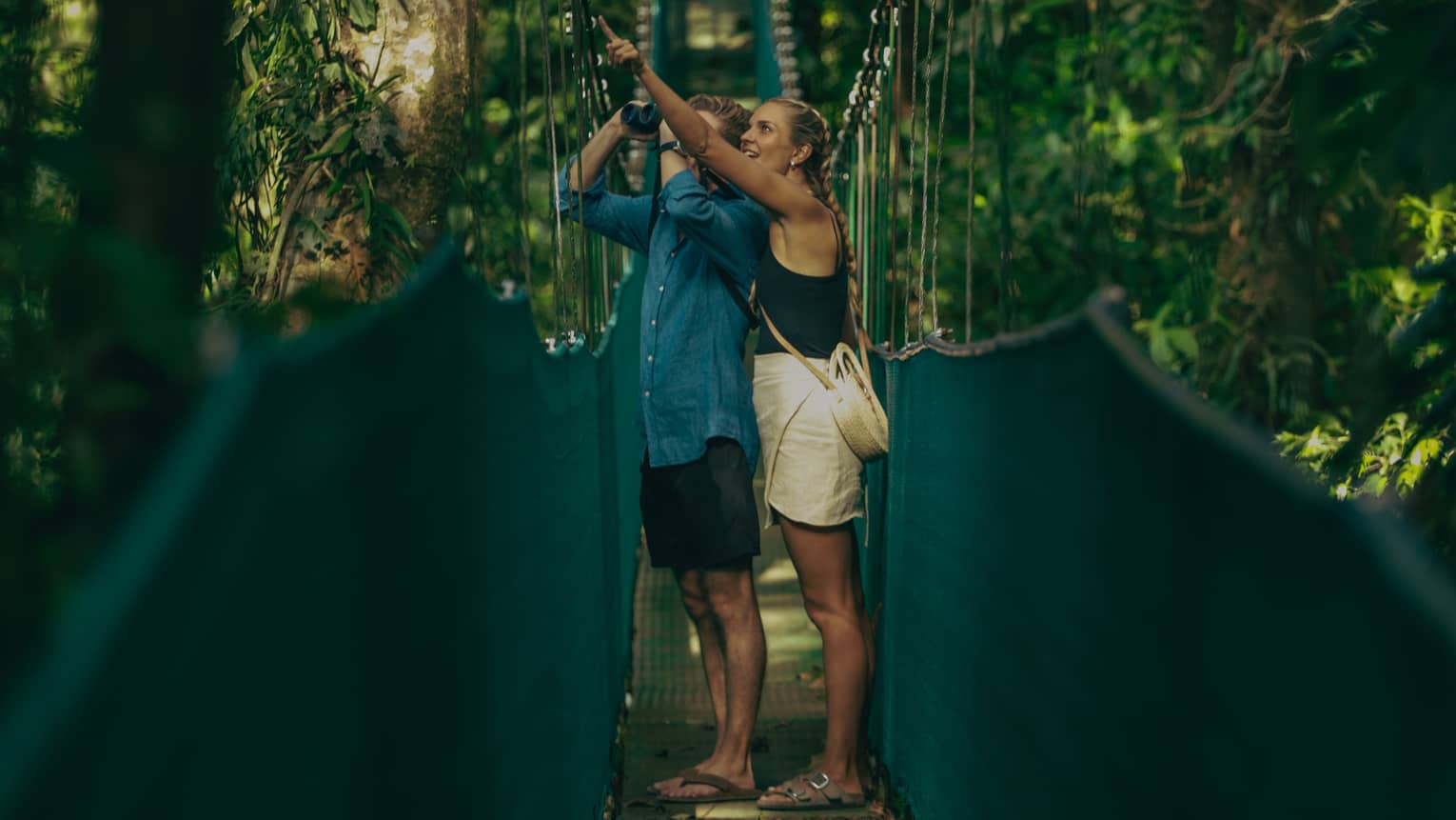 A man and woman walking along a hanging bridge.