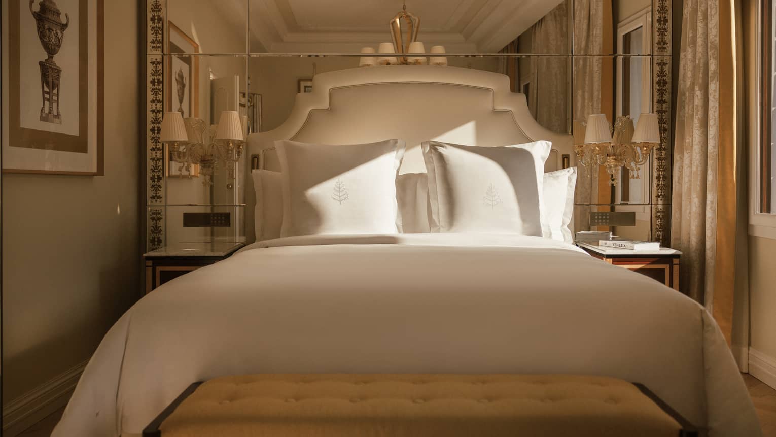 Elegant hotel room king bed with white sheets, upholstered headboard and mirrored wall