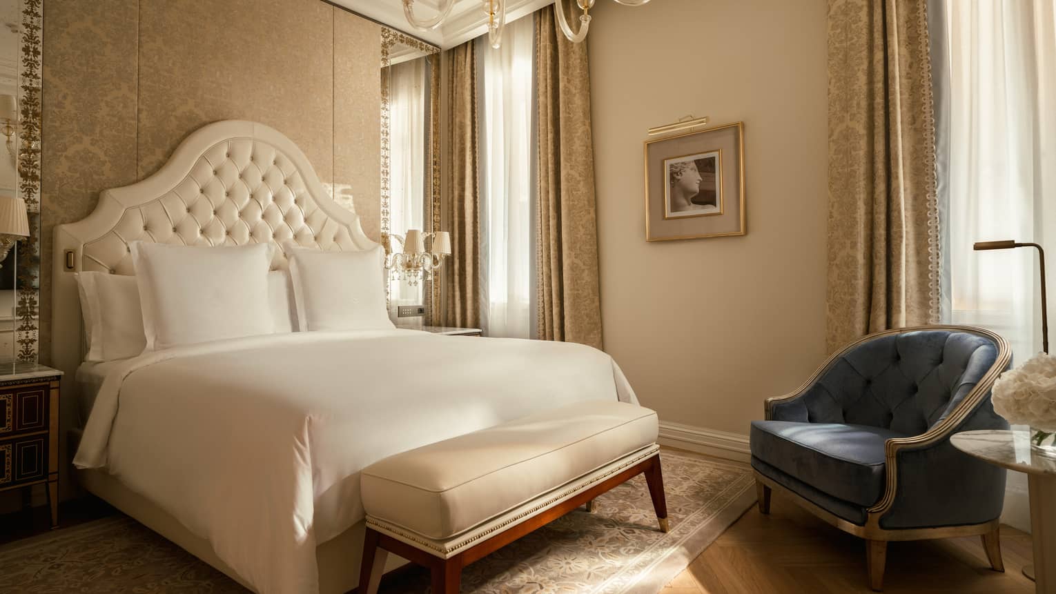 Elegant hotel bedroom featuring a king bed with white upholstered headboard and chandelier