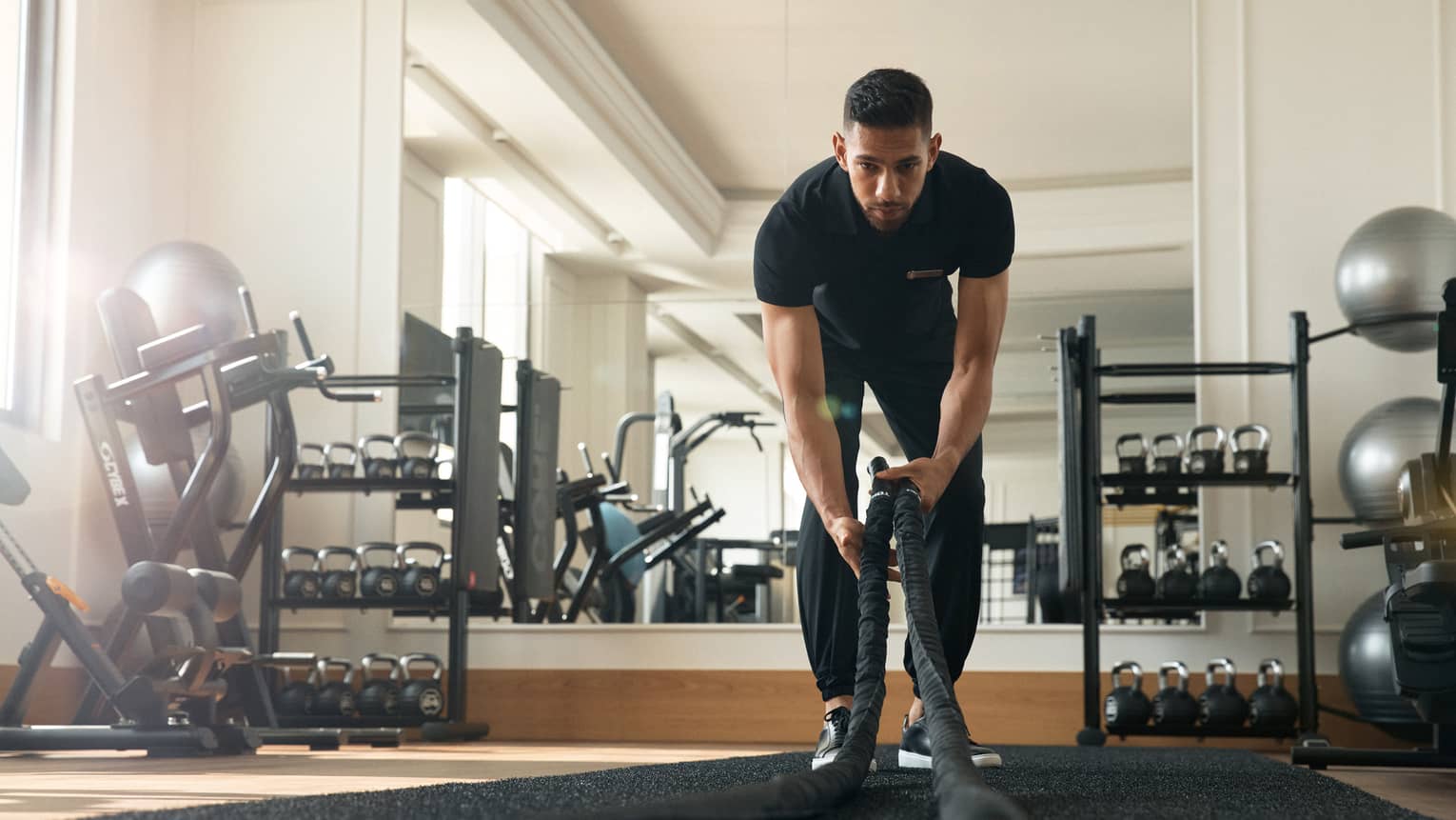 Man works out in fitness room using a heavy rope