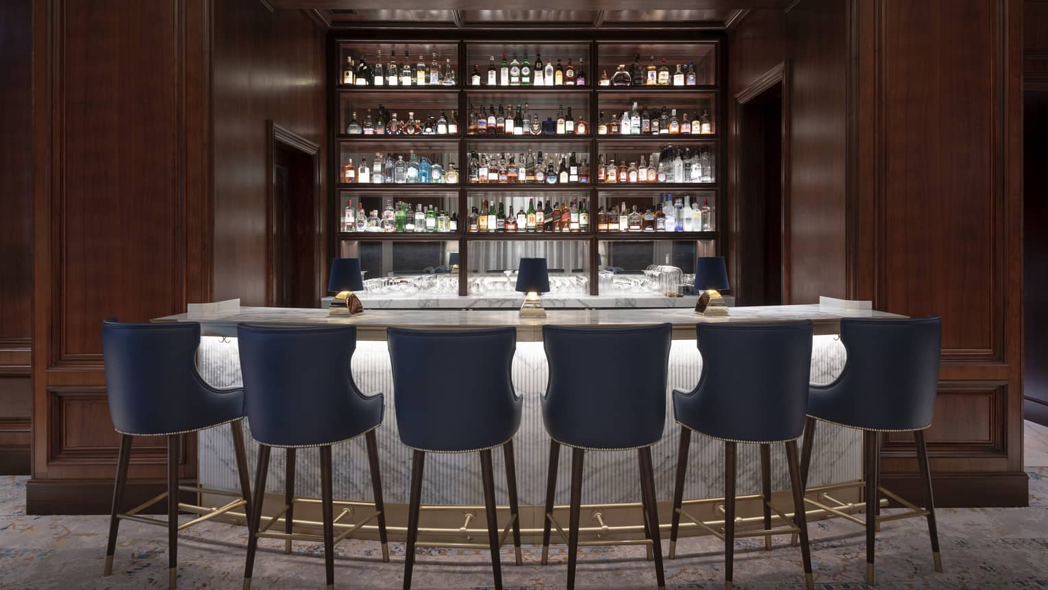 A marble bar with blue stools and wood walls.