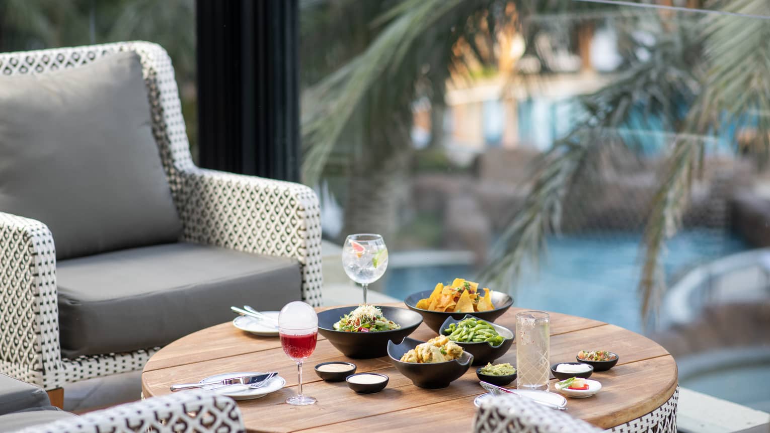 An assortment of food in black bowls and cocktails near a pool.