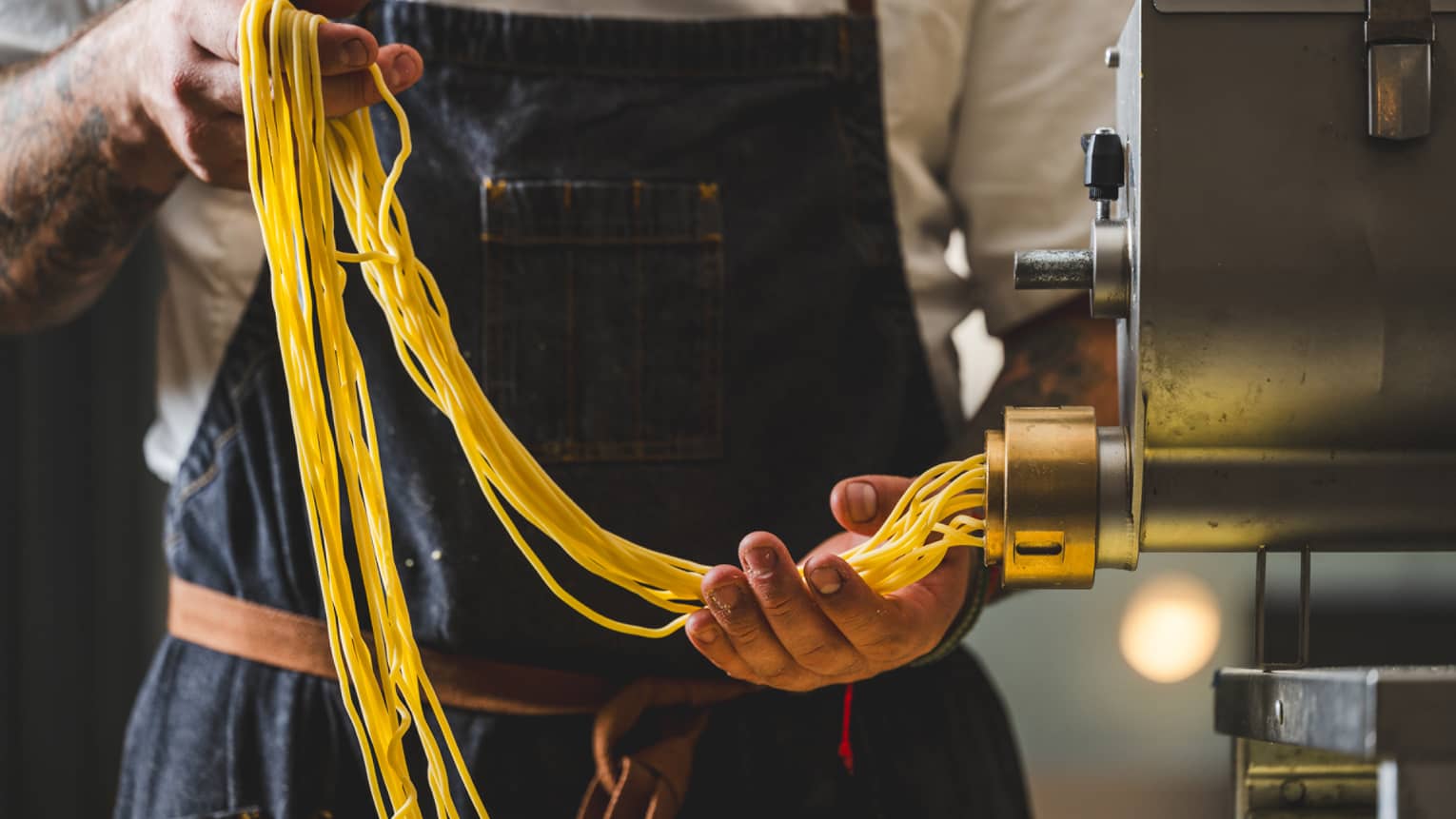 A man holds fresh pasta strands as they come out of a pasta maker