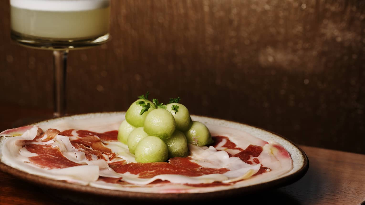 Prosciutto on a plate, topped with small green melon balls