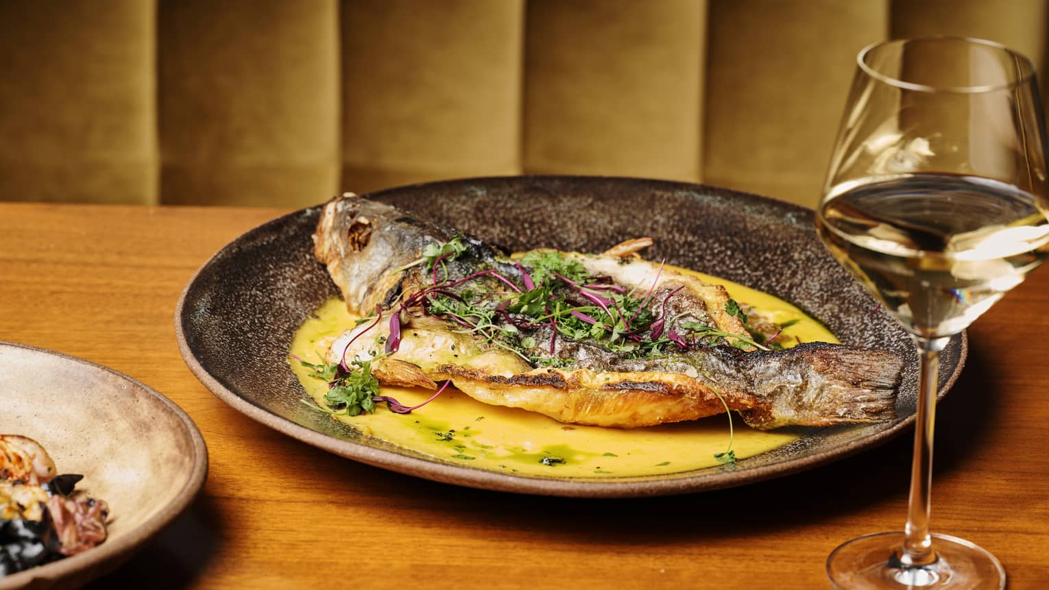 Whole fried Branzino dish and a glass of white wine on a wooden table