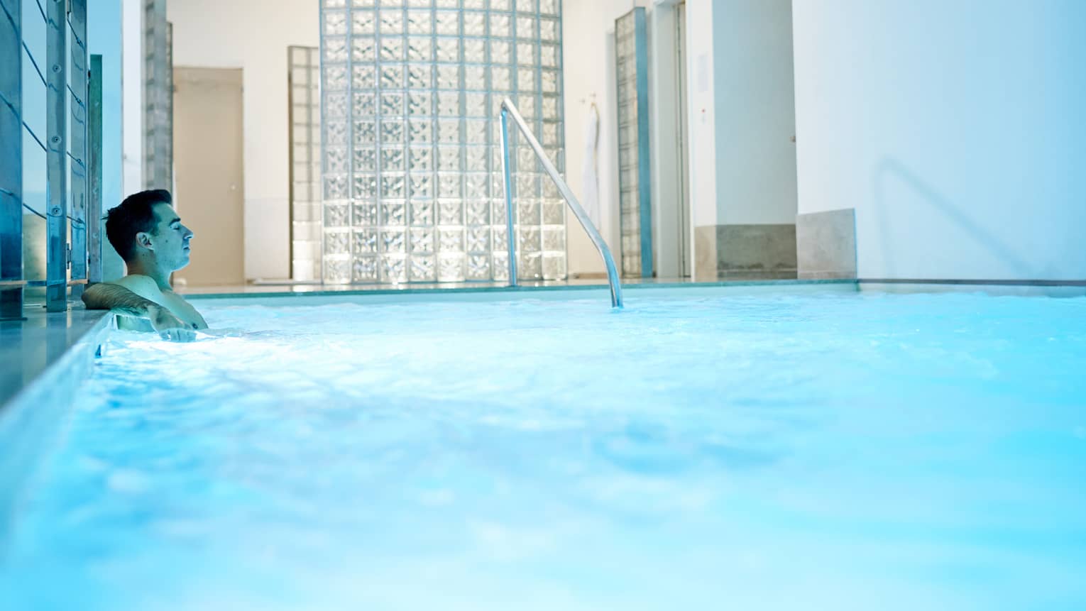 Man leans back in indoor pool with blue illuminated water