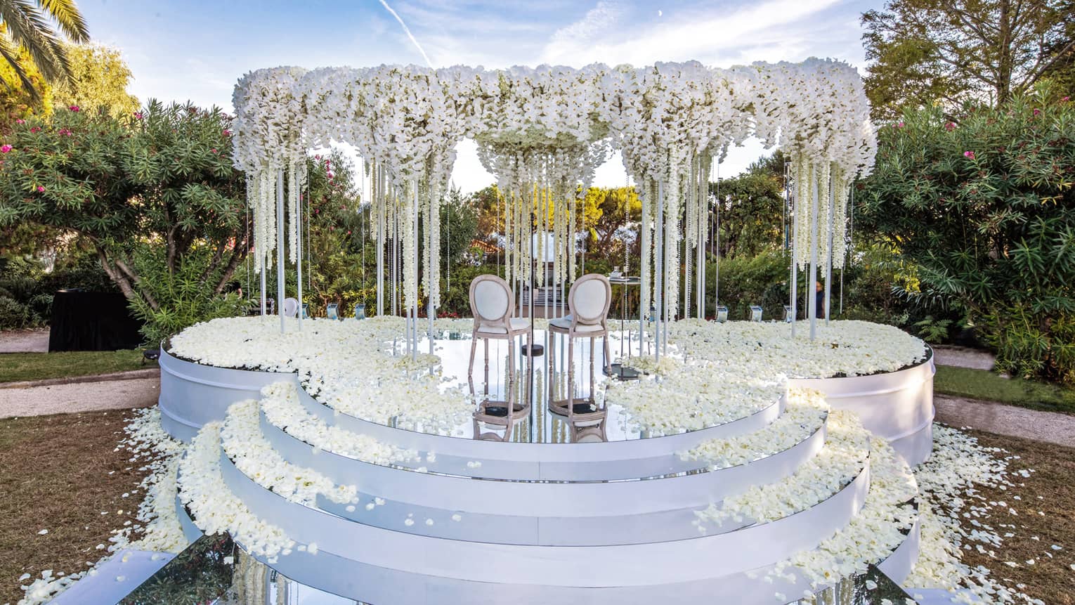 Three rounded white steps leading up to altar with arch covered in white flowers