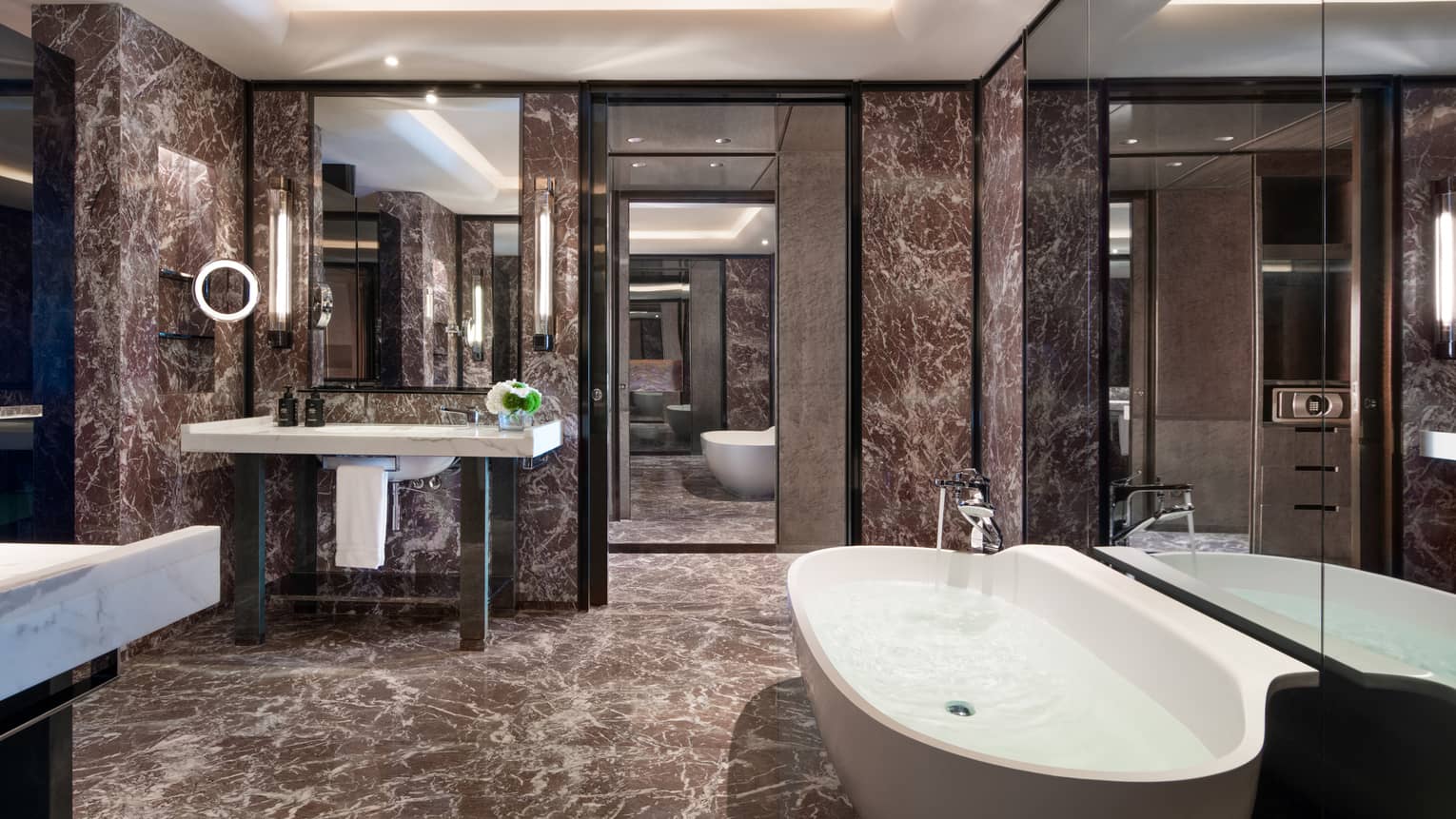 Guest bathroom with chocolate marble walls and floors, single vanity, large soaking tub, lighted wall sconces