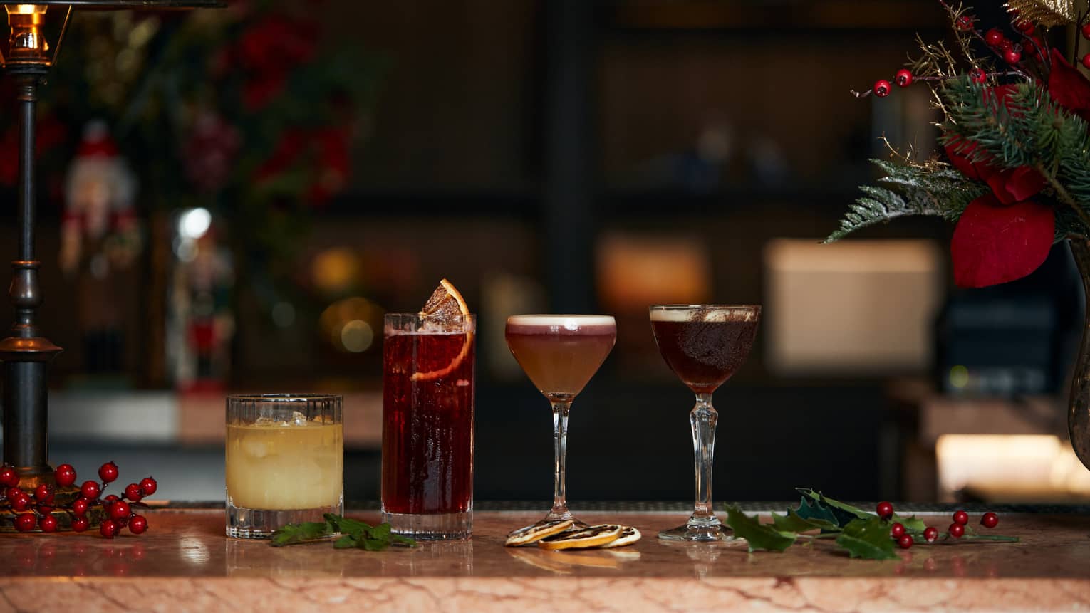 Four assorted cocktails lined up along marble bar beside holiday d�cor