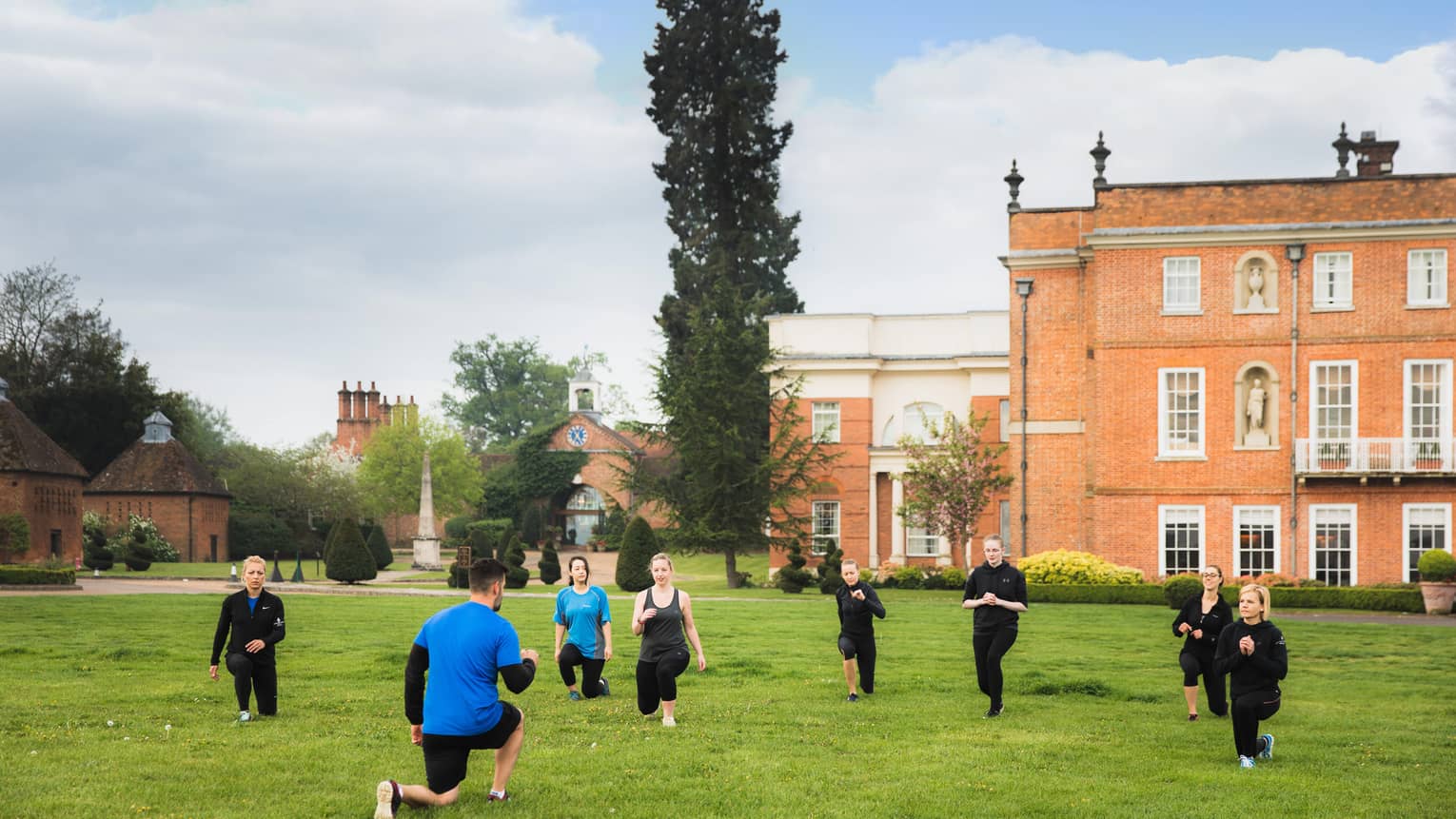 People lunge during fitness class on lawn in front of hotel building