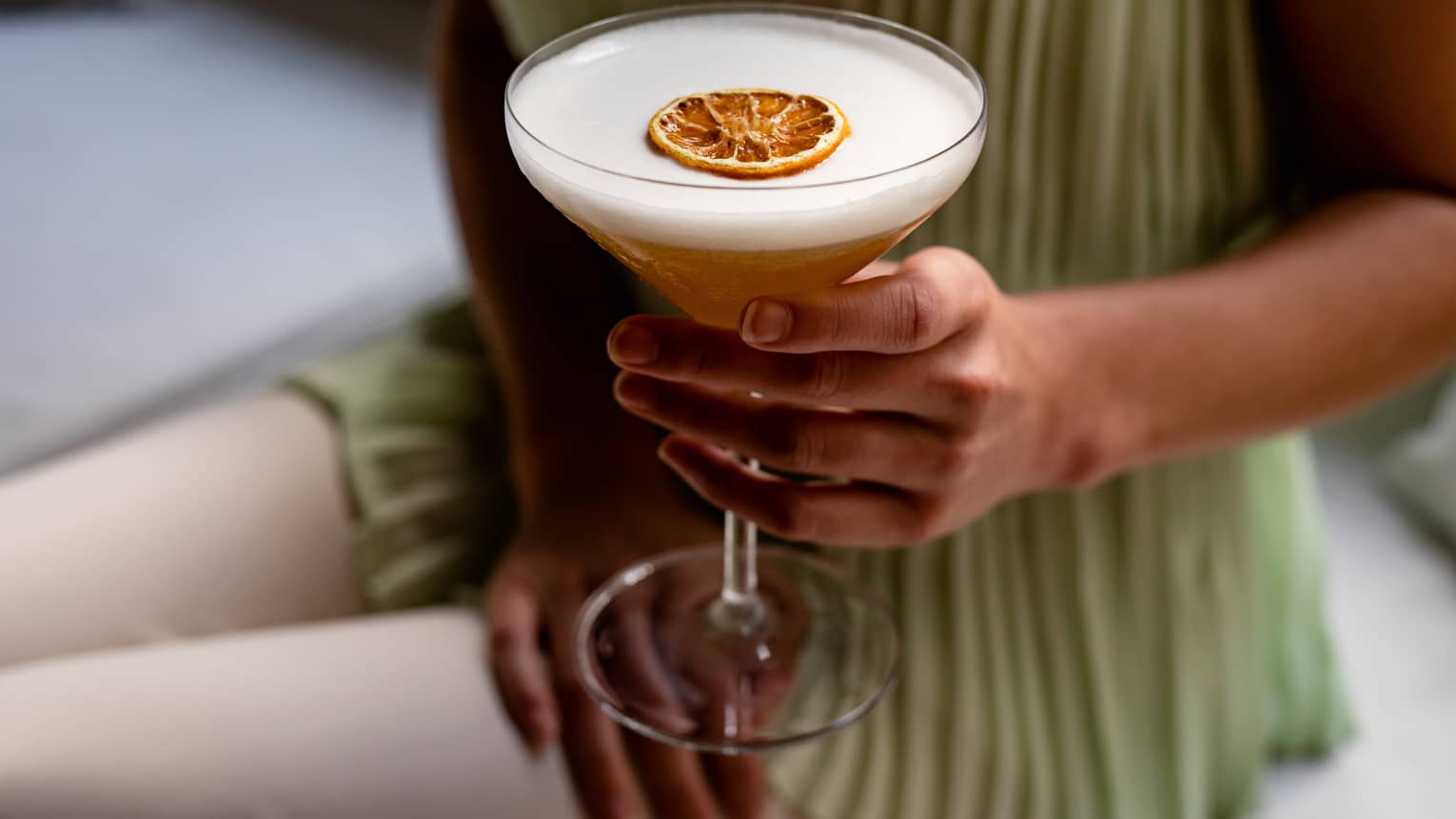 A woman's hand holds a cocktail with slide of dried orange on top