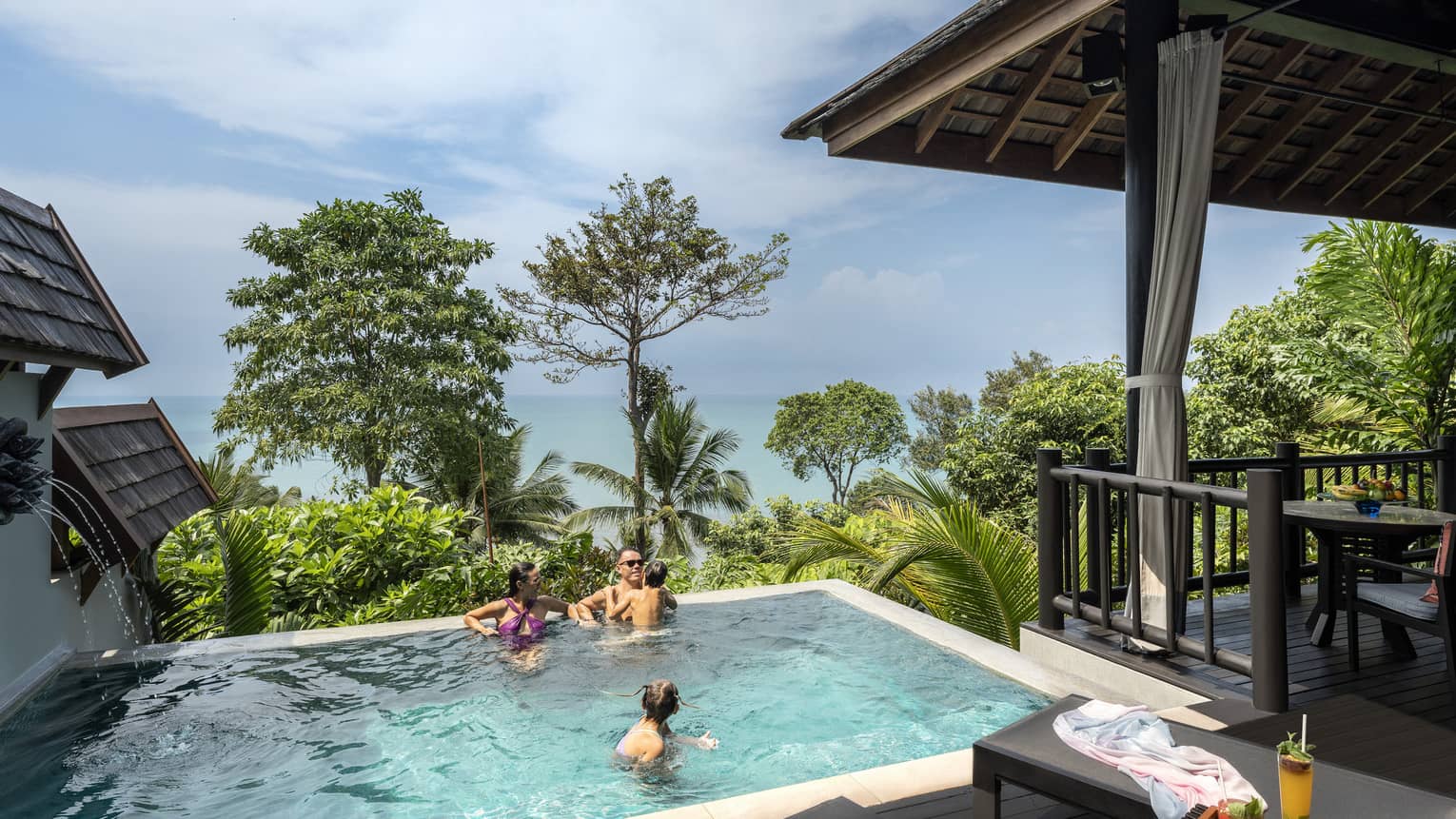 Man, woman and young boy swim in small pool overlooking trees and the sea