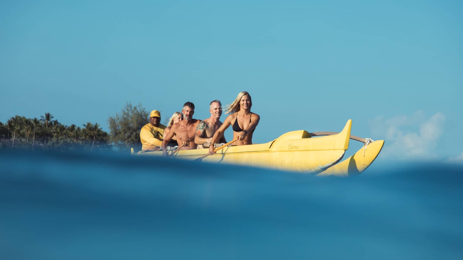 Group of friends with paddles row in large yellow canoe, Four Seasons resort staff at back