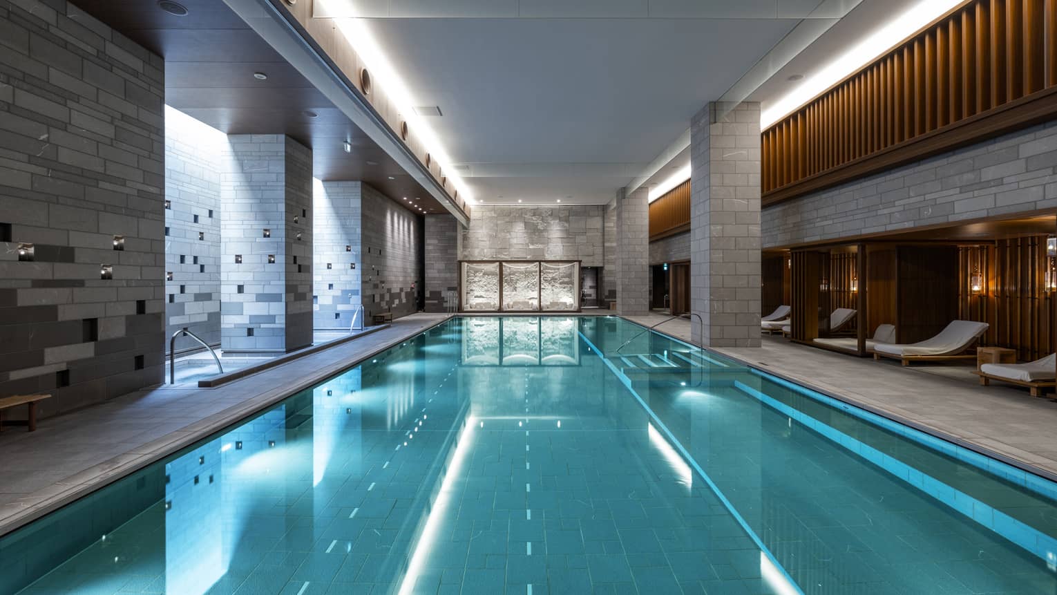 Indoor spa pool flanked by chaise longues and grey brick columns