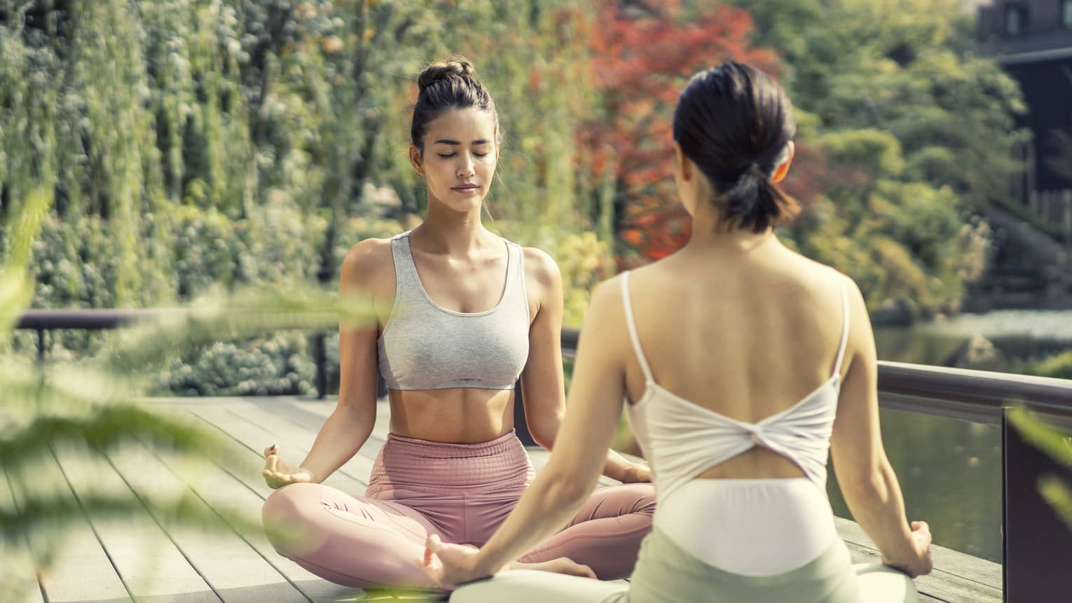 Two women sit cross-legged in a yoga pose in the Shakusui-en pond garden