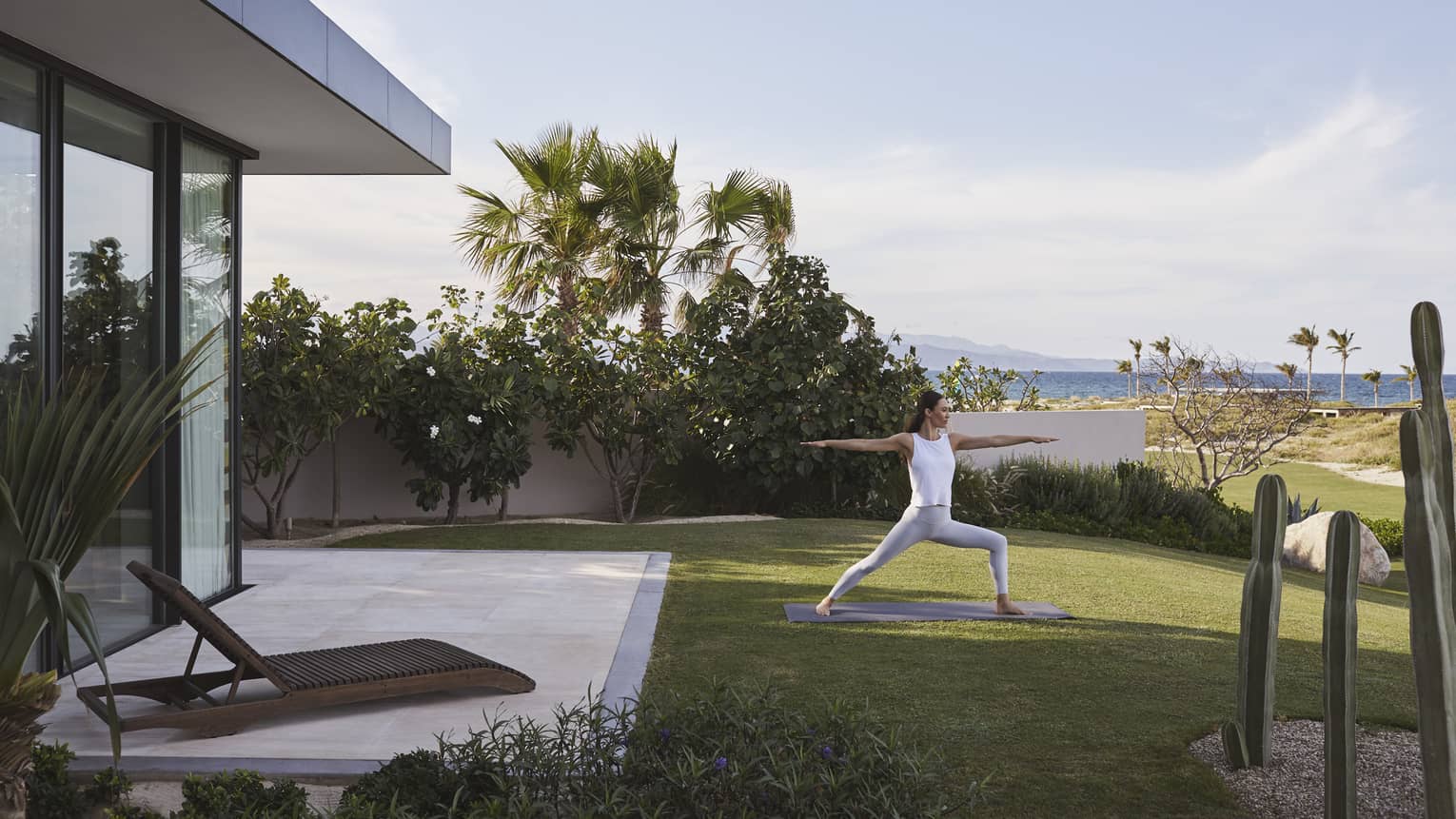 Woman doing yoga on a lawn outside her suite, with the ocean and sky in the background.