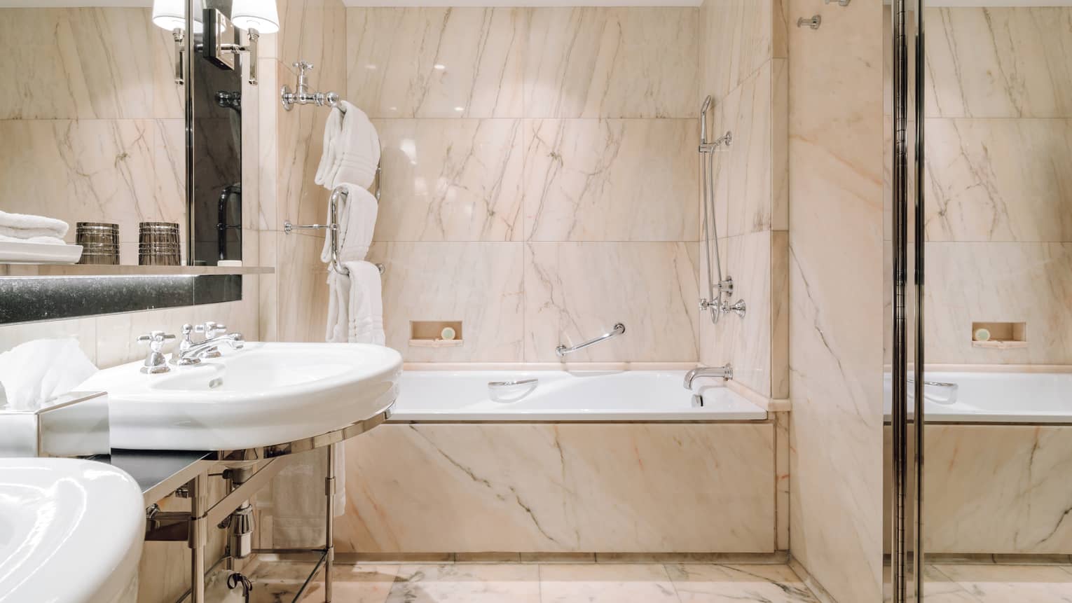 Bathroom with marble walls, a bathtub with shower, dual sinks and neatly arranged towels and bathrobes.