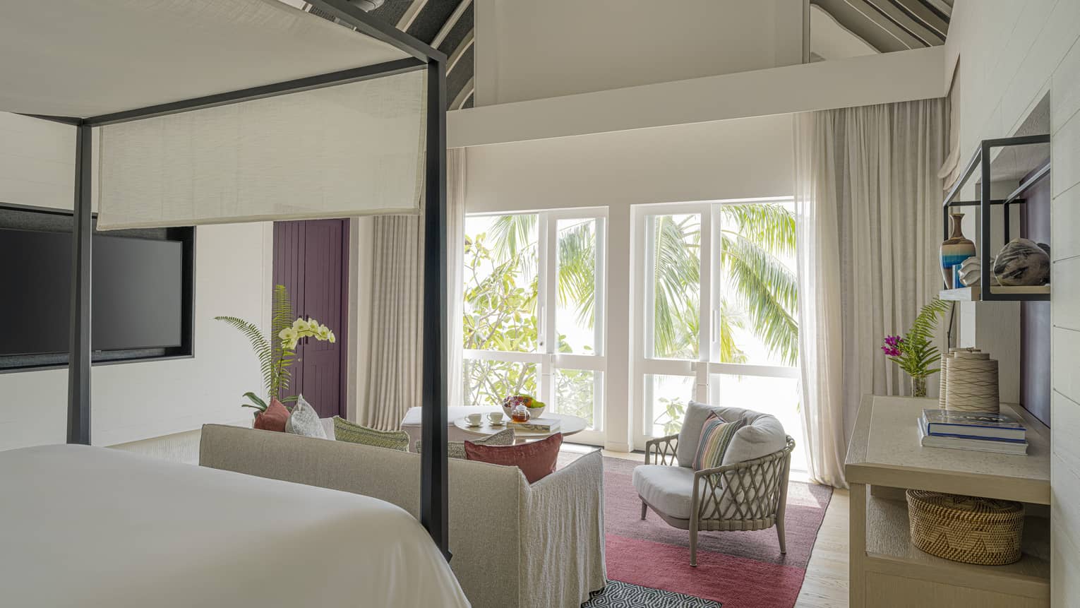 Luxury resort bedroom with four-post king bed, siting area and view of palm trees