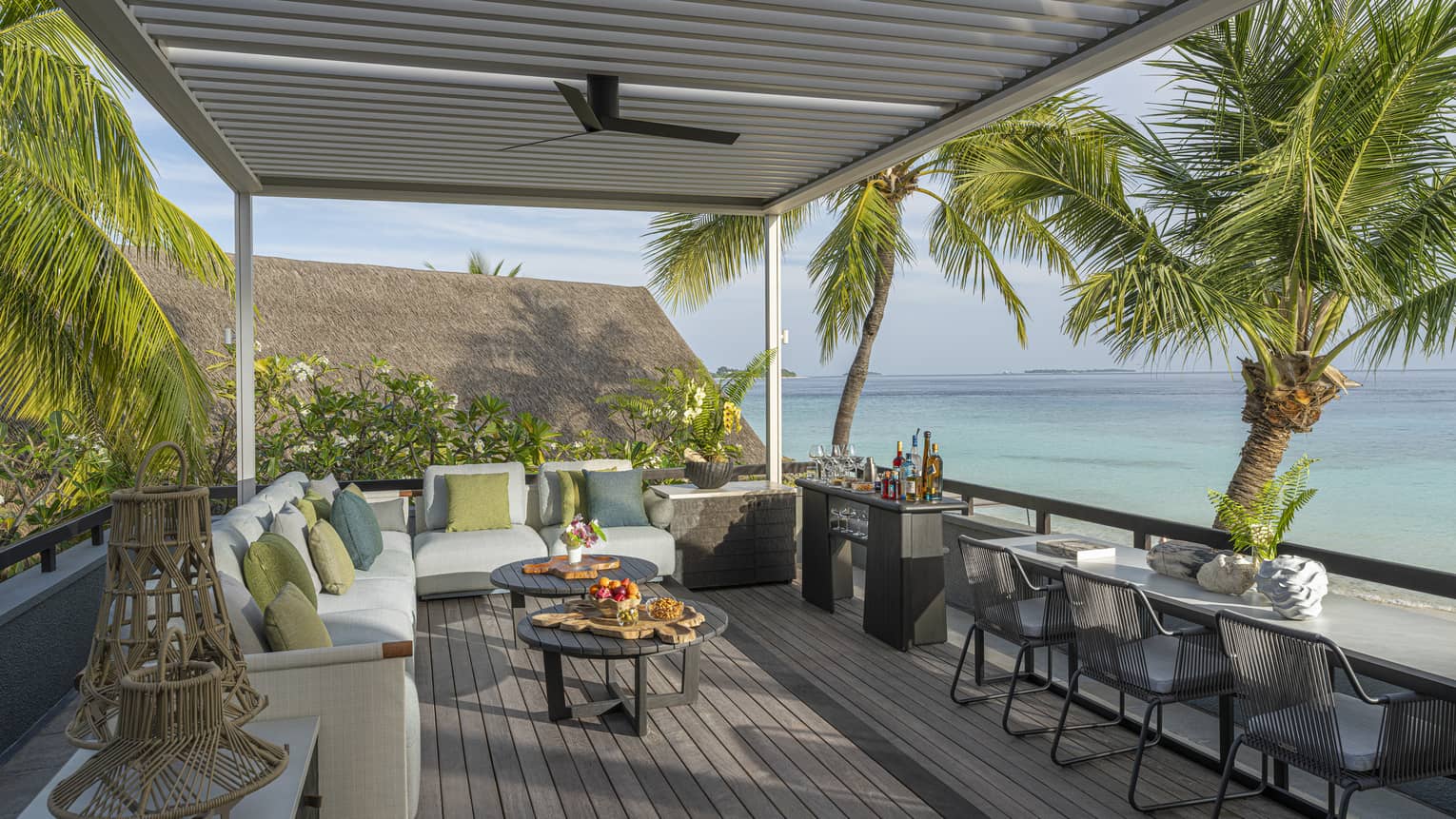 Rooftop terrace of a tropical resort estate, featuring lounge seating and three chairs at a counter ? all overlooking turquoise water