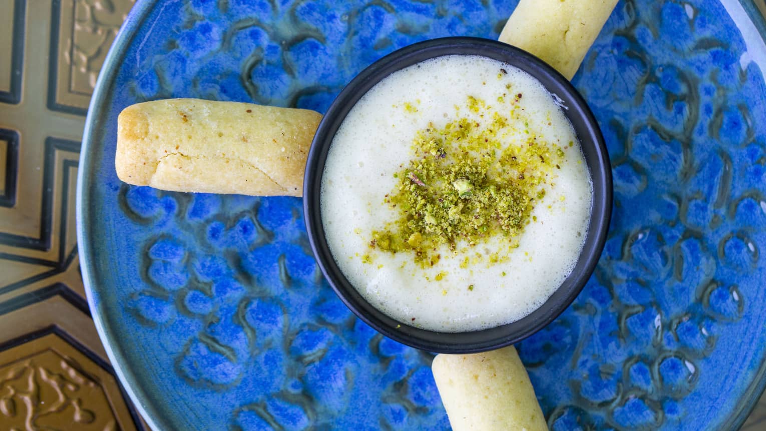 An overhead view of a white sauce with spices sprinkled on top and bread sticks around it, on a blue pottery dish