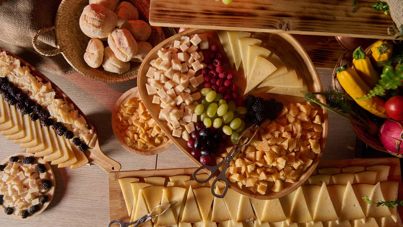 Large display of triangle-shaped cheese slices, grapes, berries, dried fruit and a basket of bread rolls