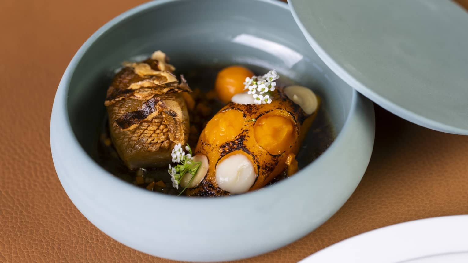 Two bright-orange roasted Jerusalem artichokes in light-blue ceramic container with lid beside it