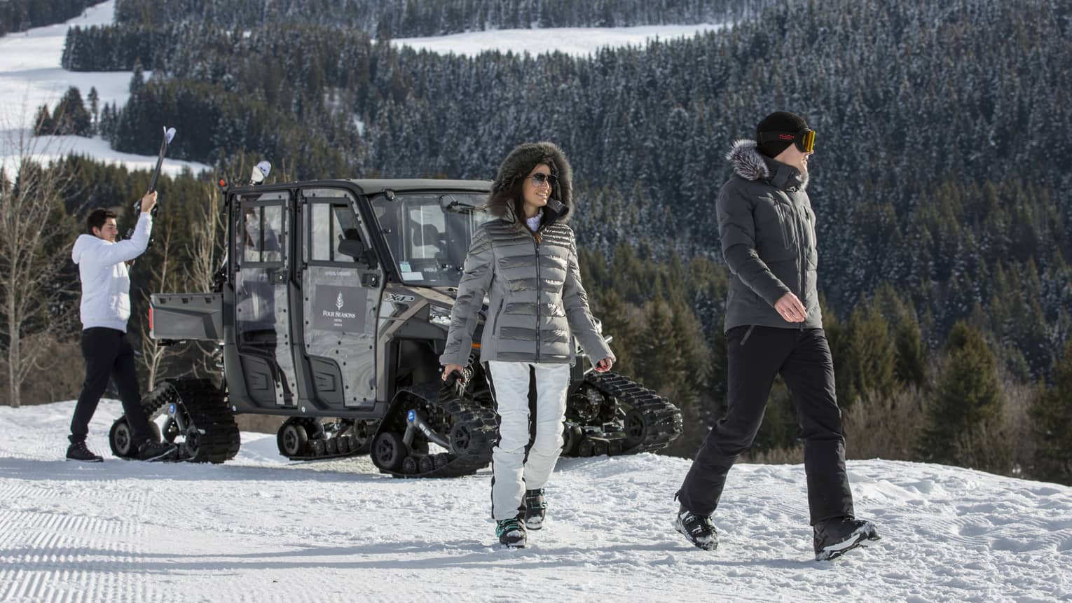 Couple walks away from ski valet large snowmobile on top of snowy mountain