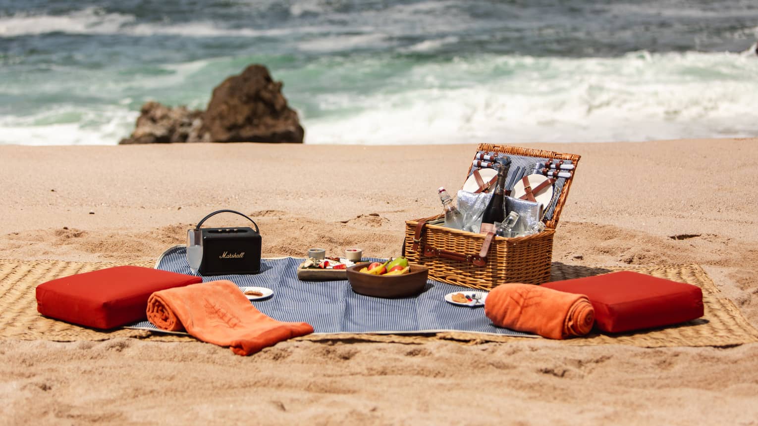 A picnic basket with cushions and a blanket on a beach.