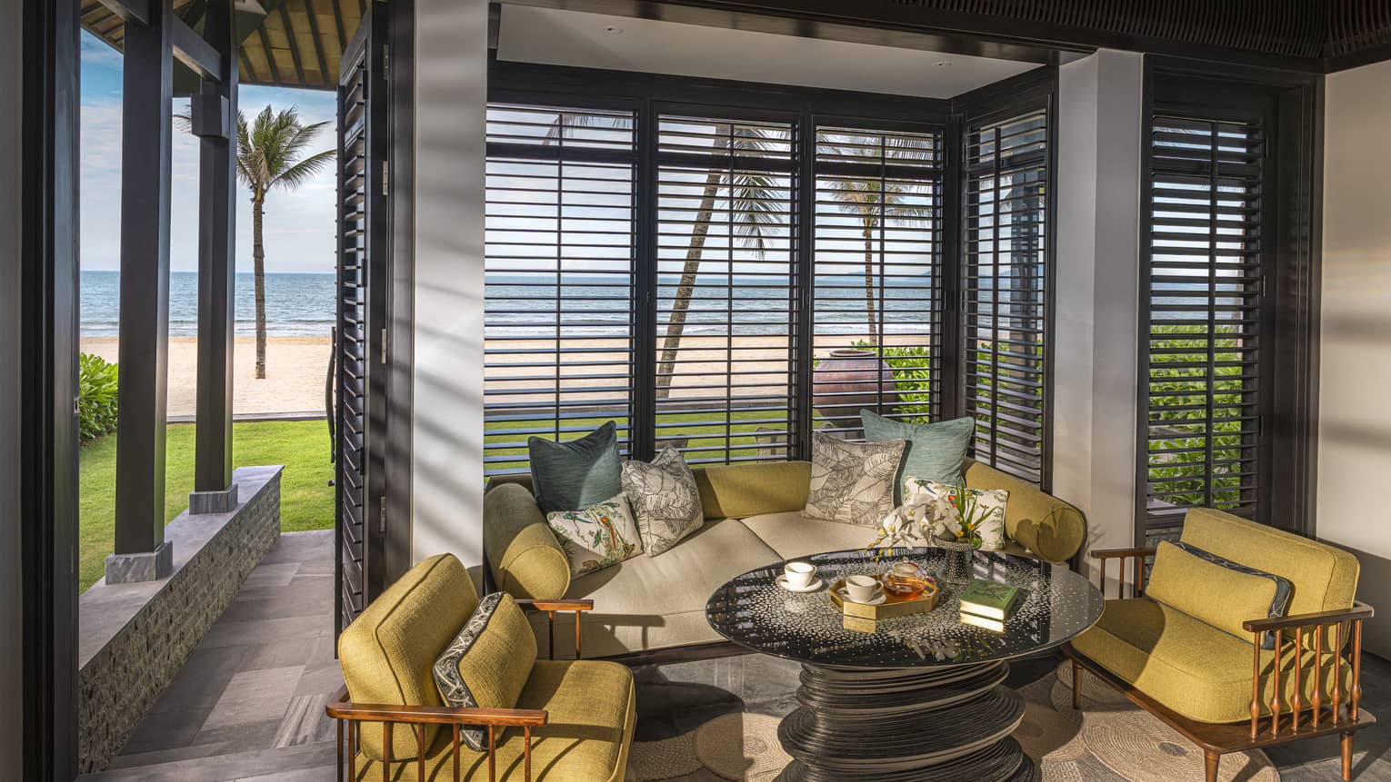 Guest room living area with mustard-coloured arm chairs, round coffee table and floor-to-ceiling windows with beach views
