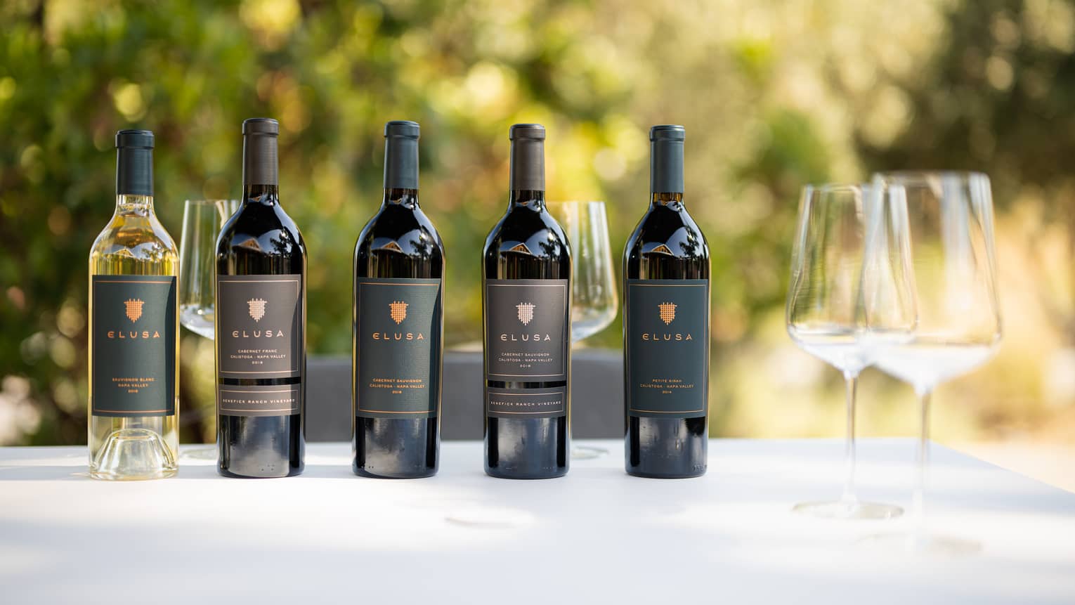 Bottles of Elusa wine on a table with wine glasses.