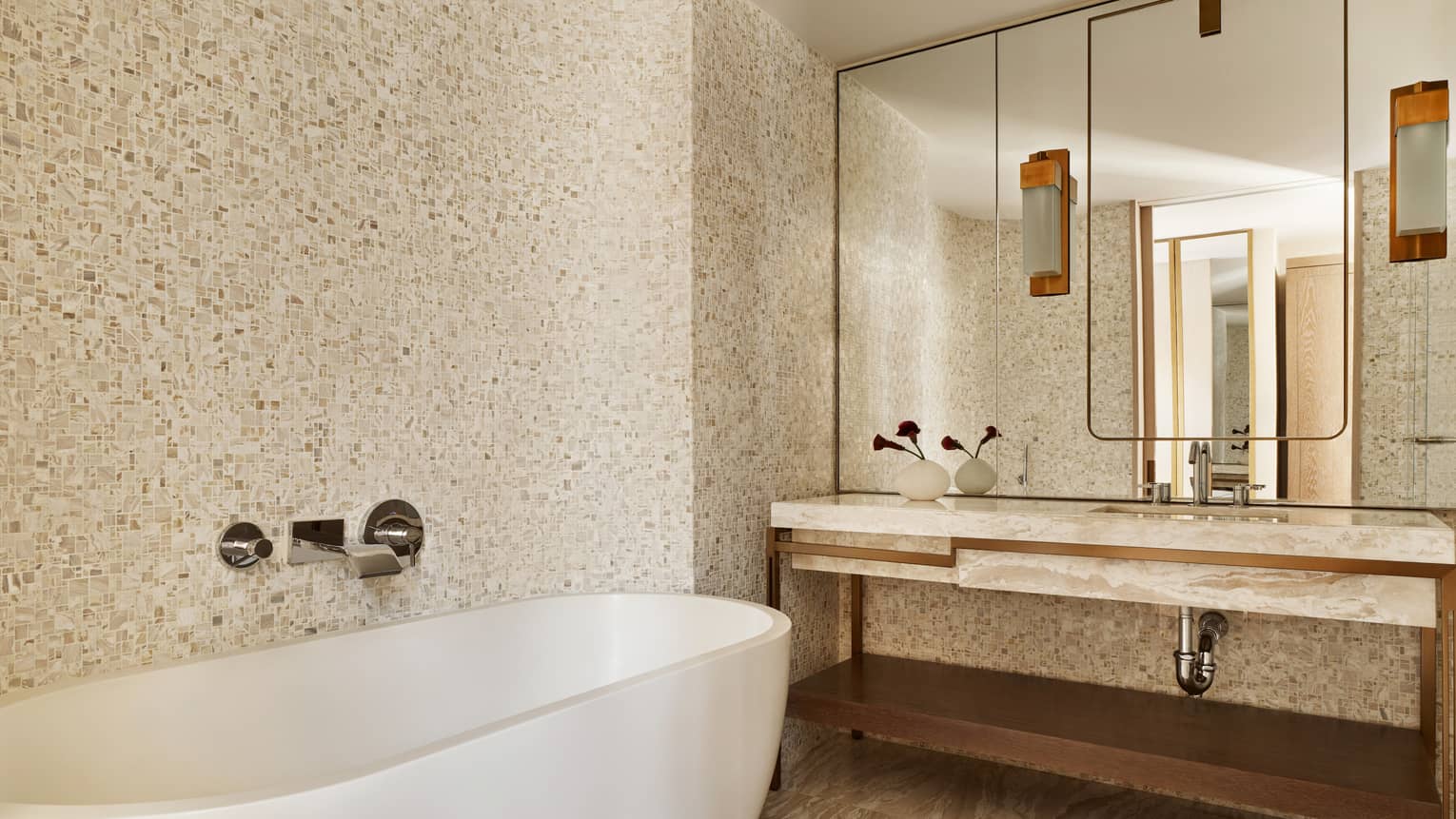 Modern hotel room bathroom with marble vanity, stone wall and freestanding oval tub