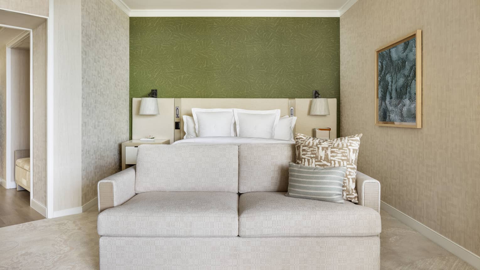 Bedroom of a resort suite, featuring a king bed, green accent wall, and a two-seater sofa at the foot of the bed