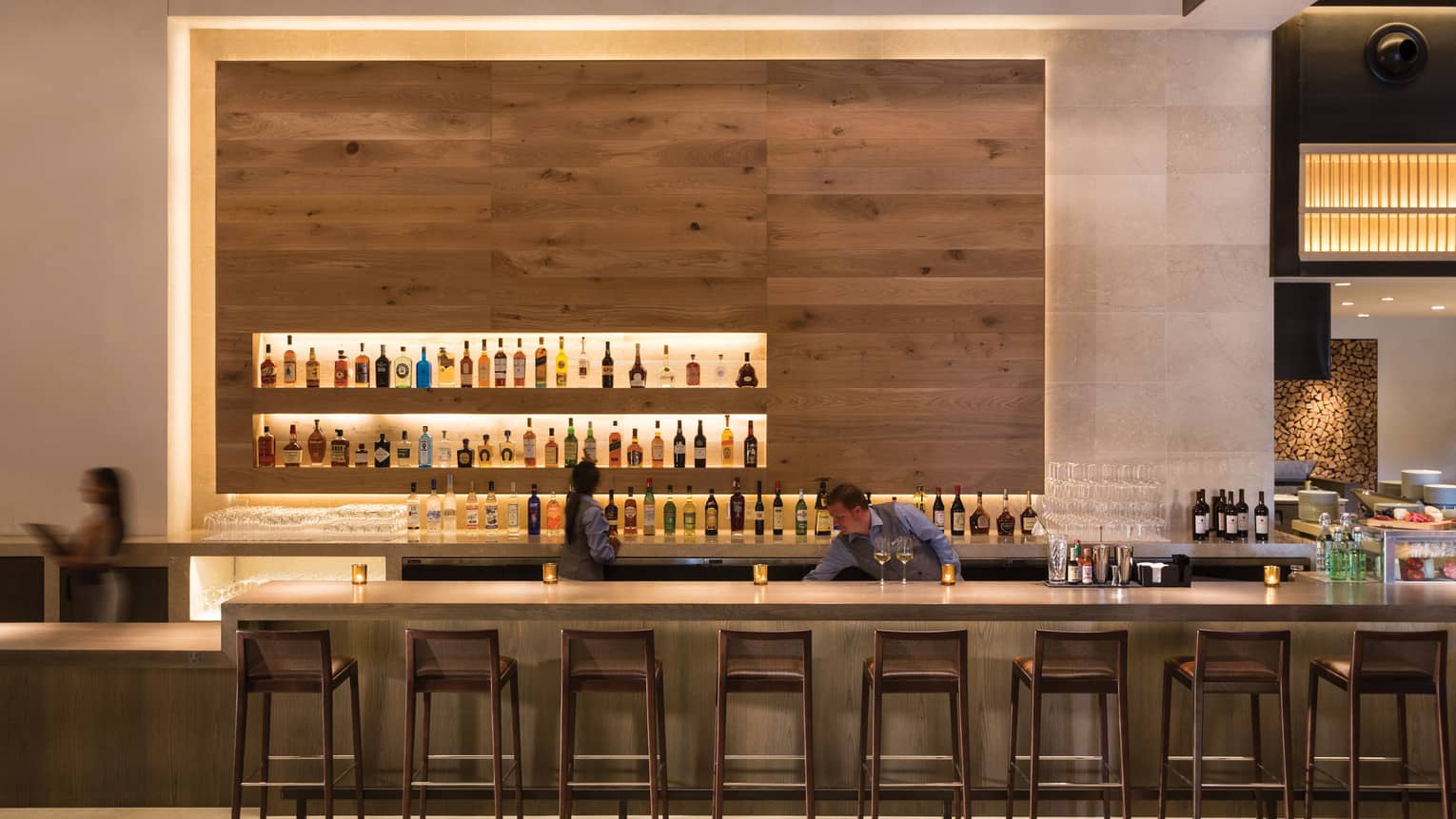 A bar with many barstool and three workers cleaning and organizing the large number of bottles behind the bar.