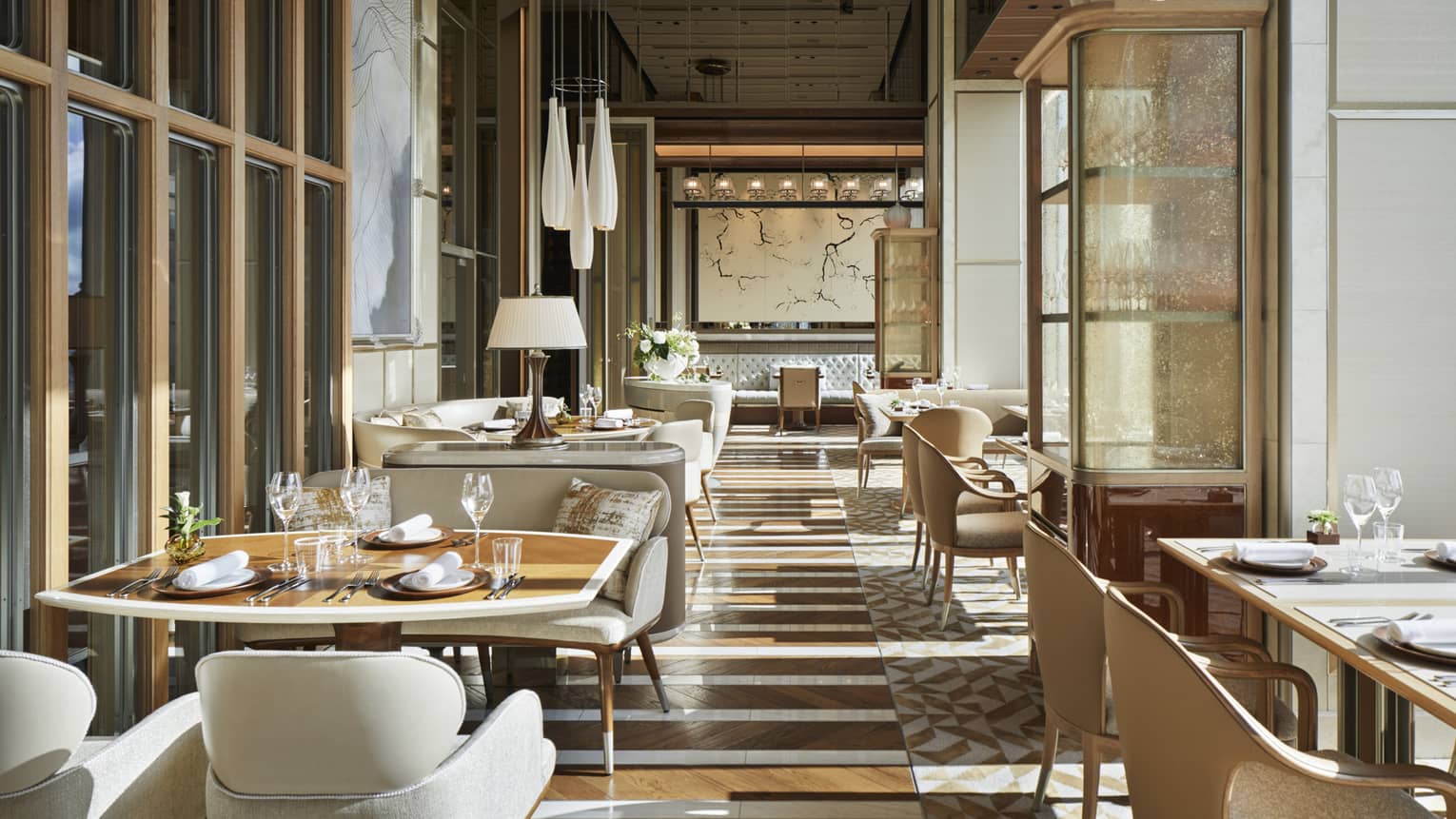 Est dining room with cream plush chairs, tables set with glassware, natural light, hardwood floors 