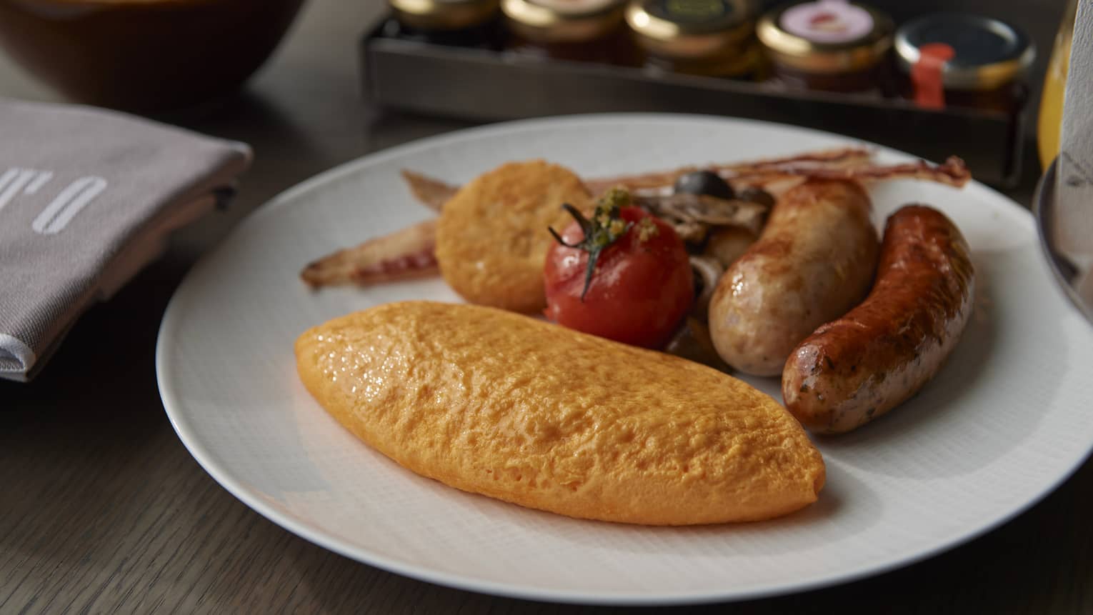 A white plate of different types of sausages , a tomato, root vegetables, and omelette.