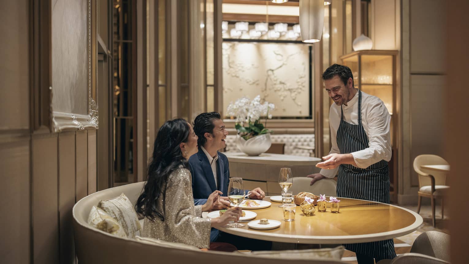 Couple dines at circular table at est, sommelier presenting them with a bottle of wine