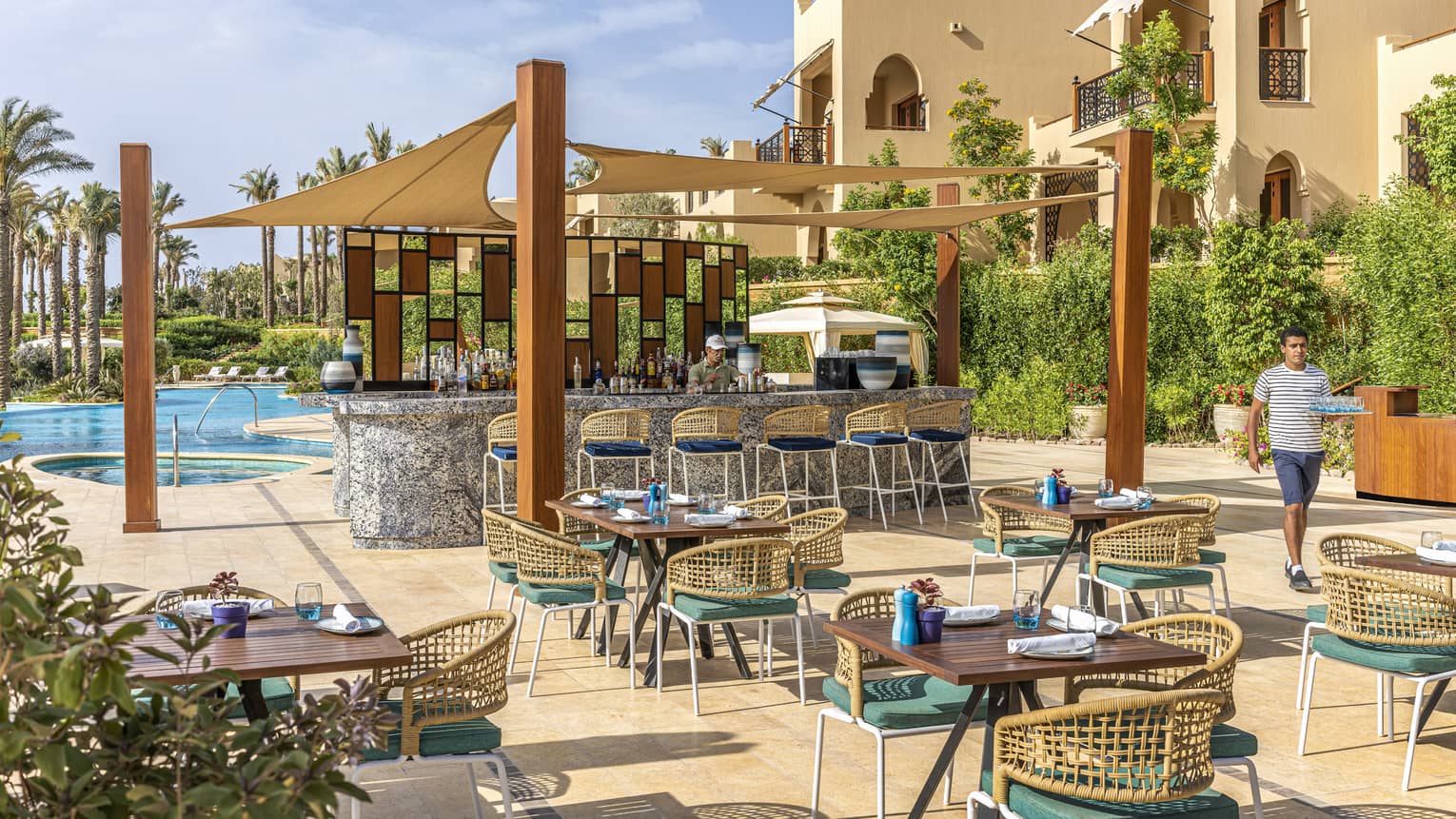 Poolside Luna restaurant with staff member walking past covered bar and intimate seating