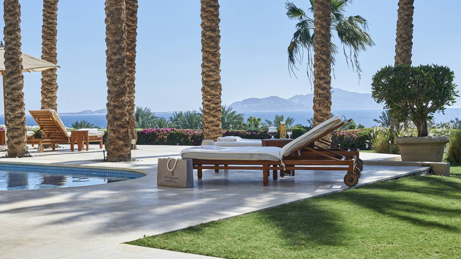 Pool terrace lounge chairs, palm trees and sea view