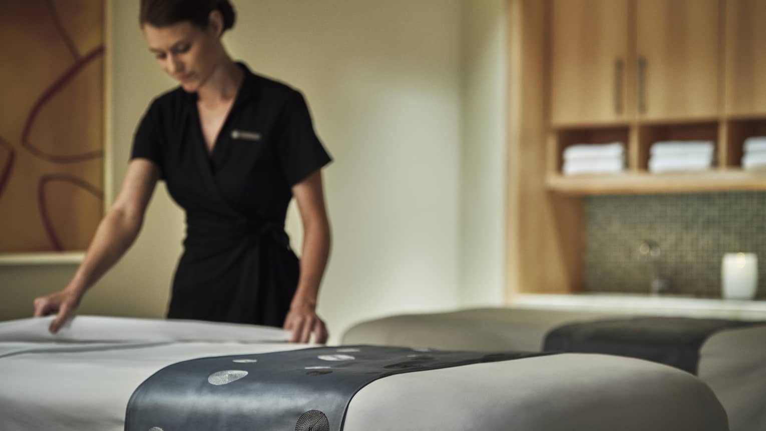 Spa attendant in black dress folds down white sheet on massage table
