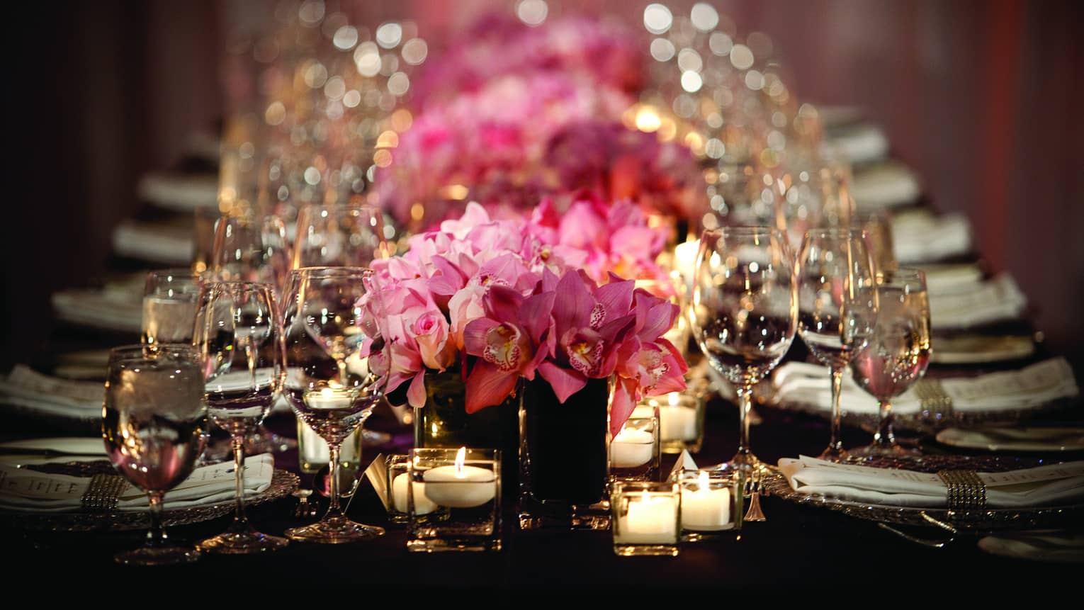 Pink roses, empty wine glasses and glowing candles line long dining table