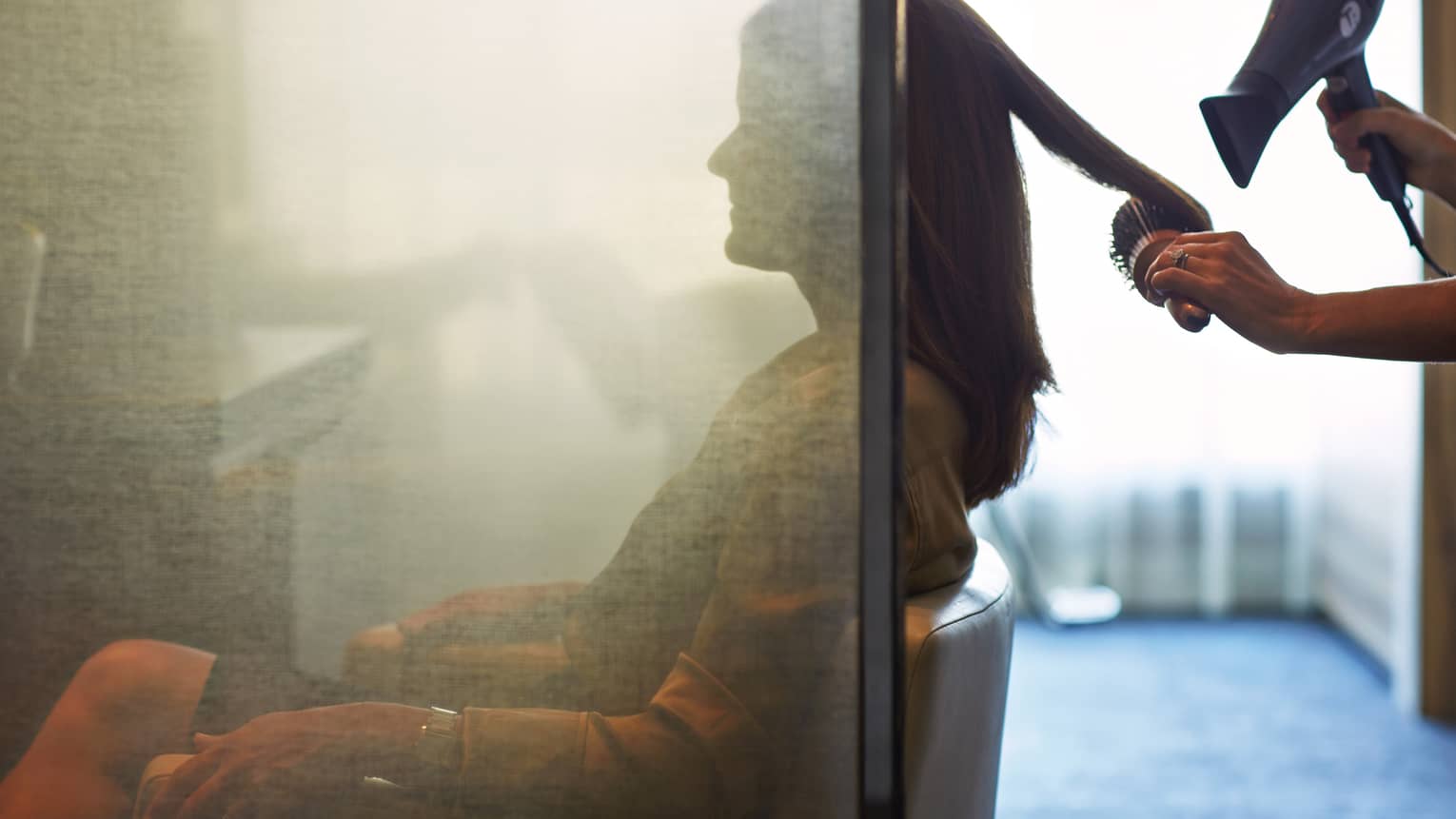 Silhouette of woman behind salon screen as hairdressers brushes, blow dries hair