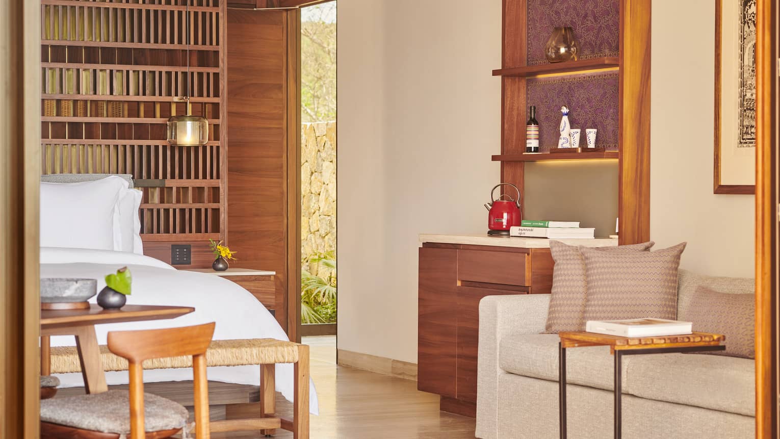 A warm, inviting suite featuring a plush bed with a wooden lattice headboard, a small sofa and a side table. A built-in shelf holds a red kettle and decorative items.
