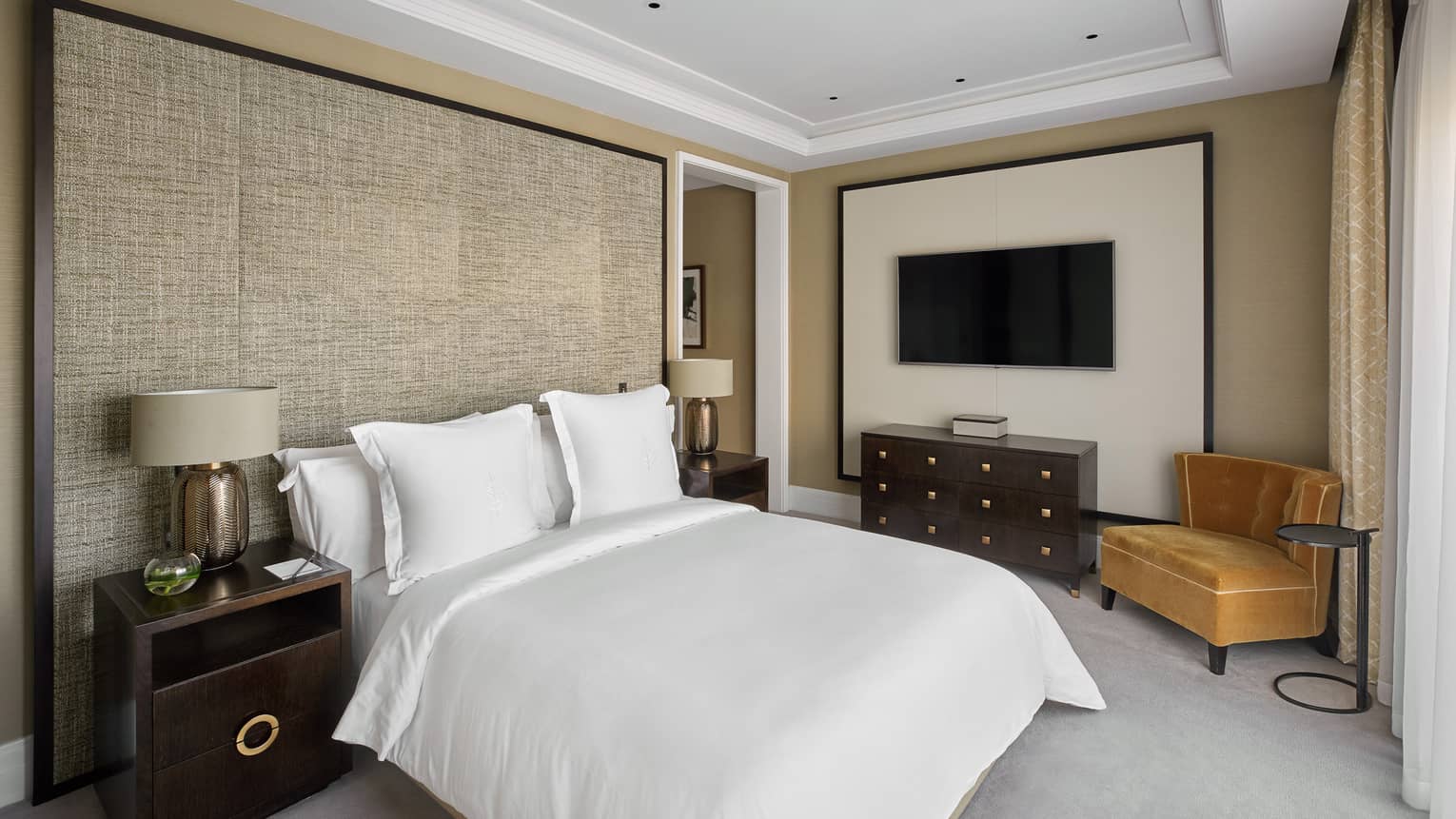 A room with a bed, cabinet, two side tables with lamps and a chair.