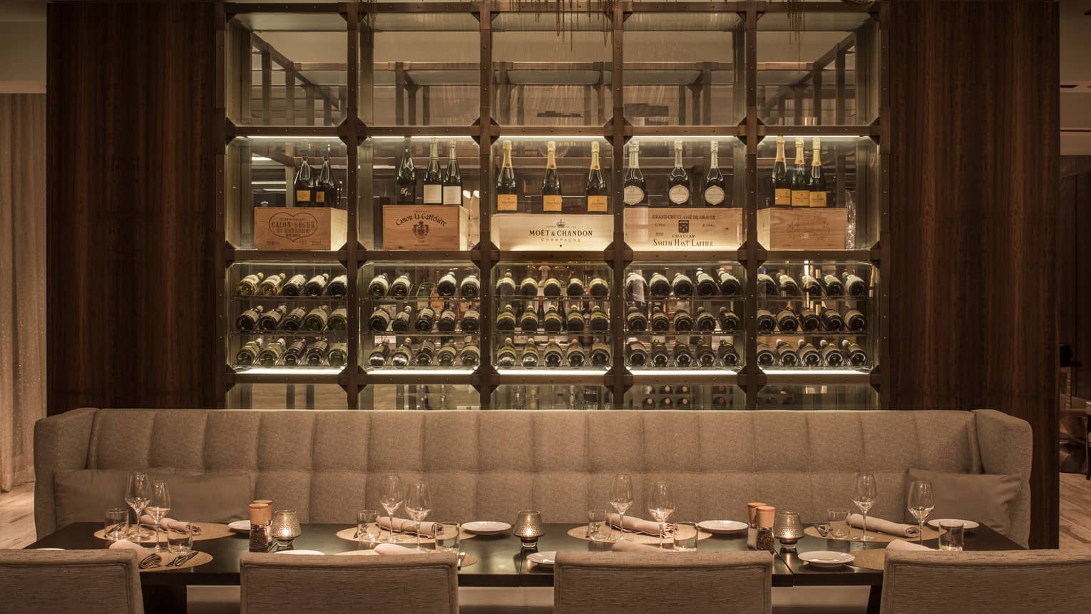 Long beige banquette along dining set dining table with glassed wine cellar in back