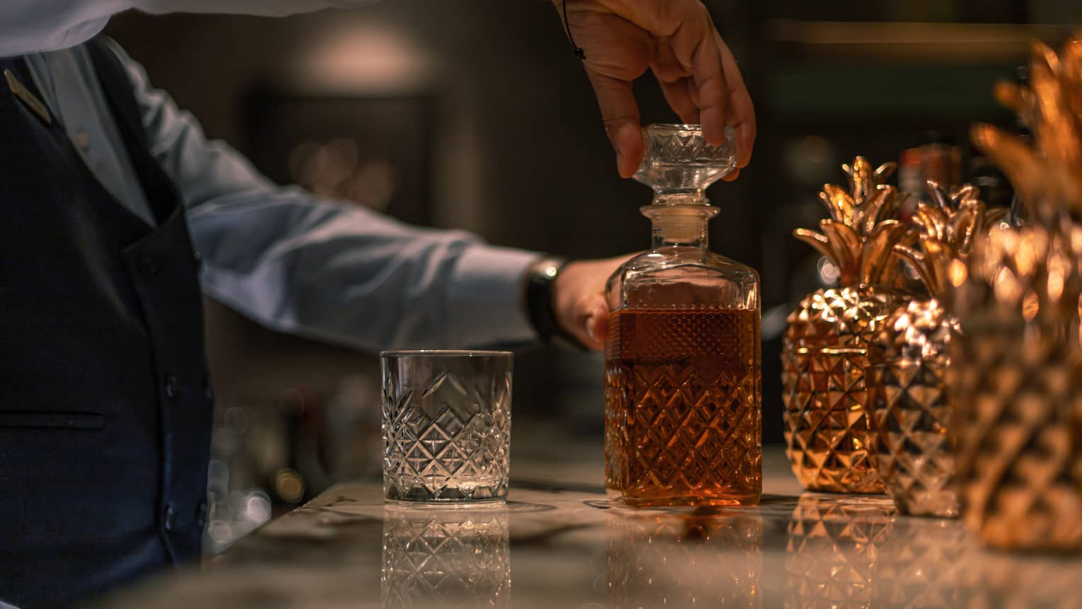 Bartender taking off bottle stopper from liquor-filled crystal decanter