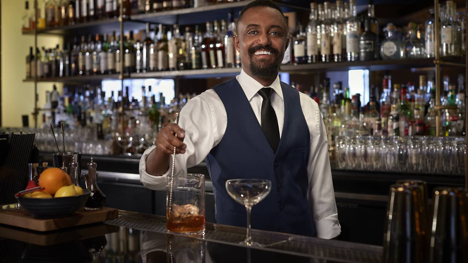 A bartender making a cocktail in front of a wall full of alcohol and drinks.