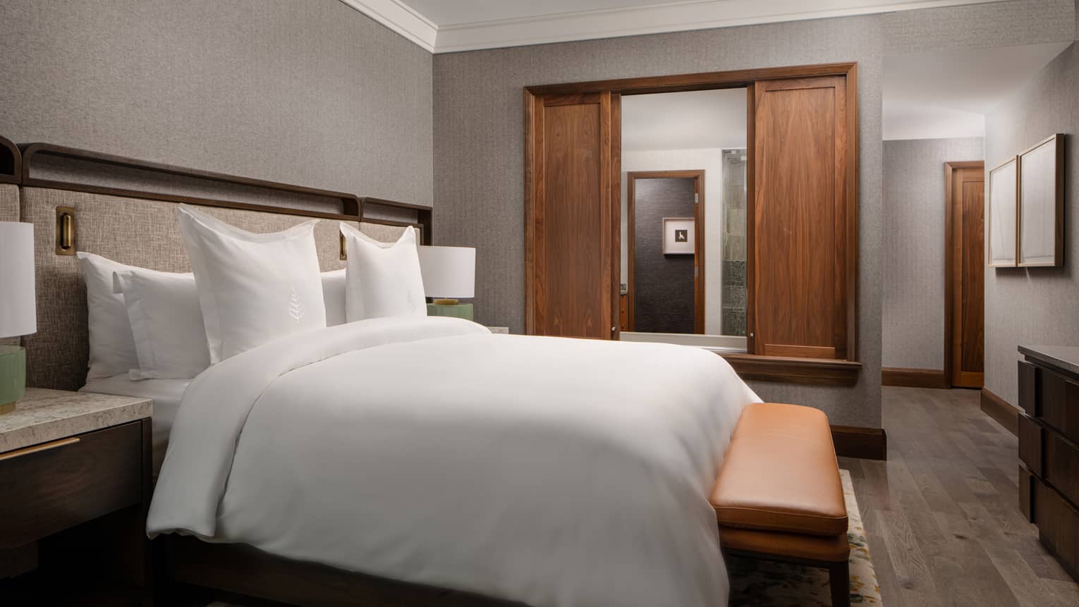Bedroom with king bed, bench, sliding wooden doors to bathroom