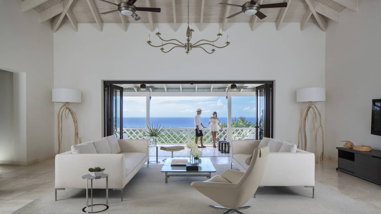 Living room with modern white furniture in front of open doors to sunny patio, couple